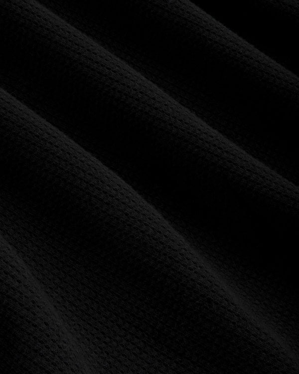 Black mesh muscle tank with diagonal folds, creating shadows and a subtle waffle texture across the surface.
