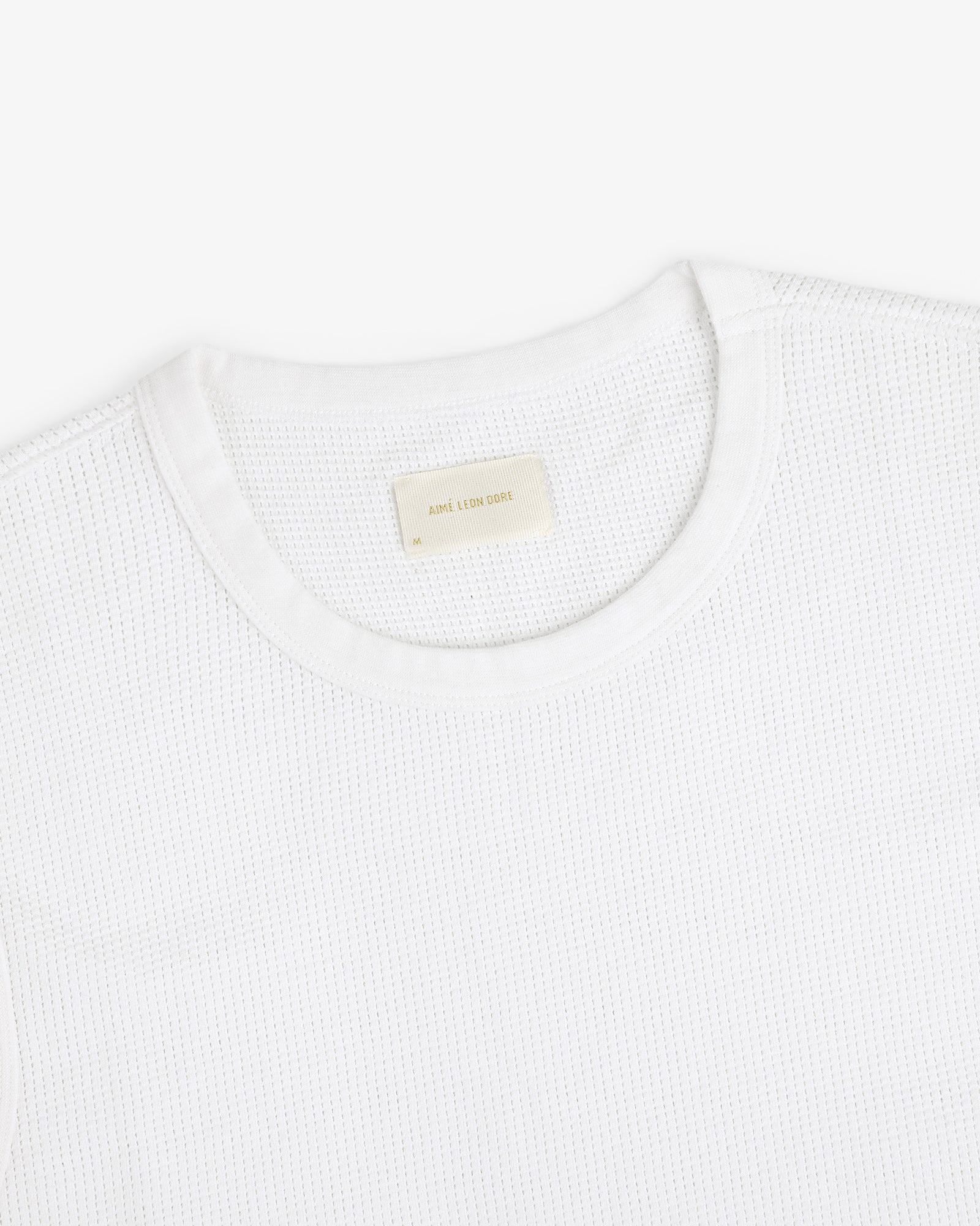 A close-up of a white Mesh Muscle Tank with a beige label inside the collar.