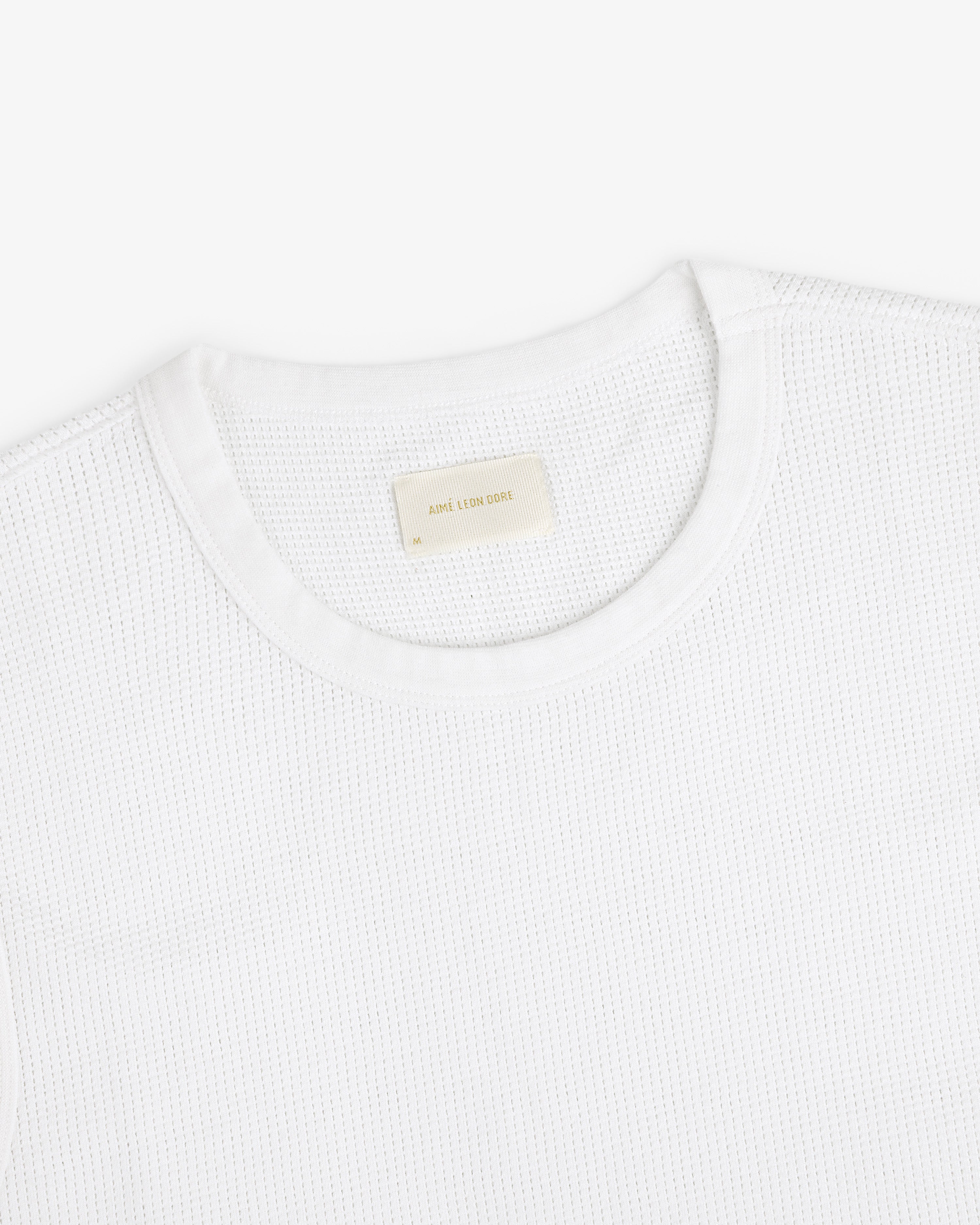 A close-up of a white Mesh Muscle Tank with a beige label inside the collar.