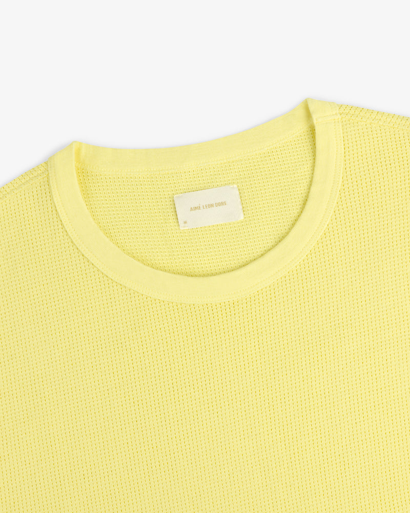 A close-up of a light yellow Mesh Muscle Tank with a blank neck label on a plain background.
