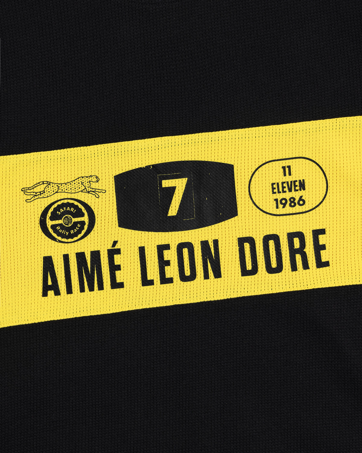 Close-up of the Long-Sleeve Rally Tee in black with a yellow stripe, AIMÉ LEON DORE logos, and the number 7.