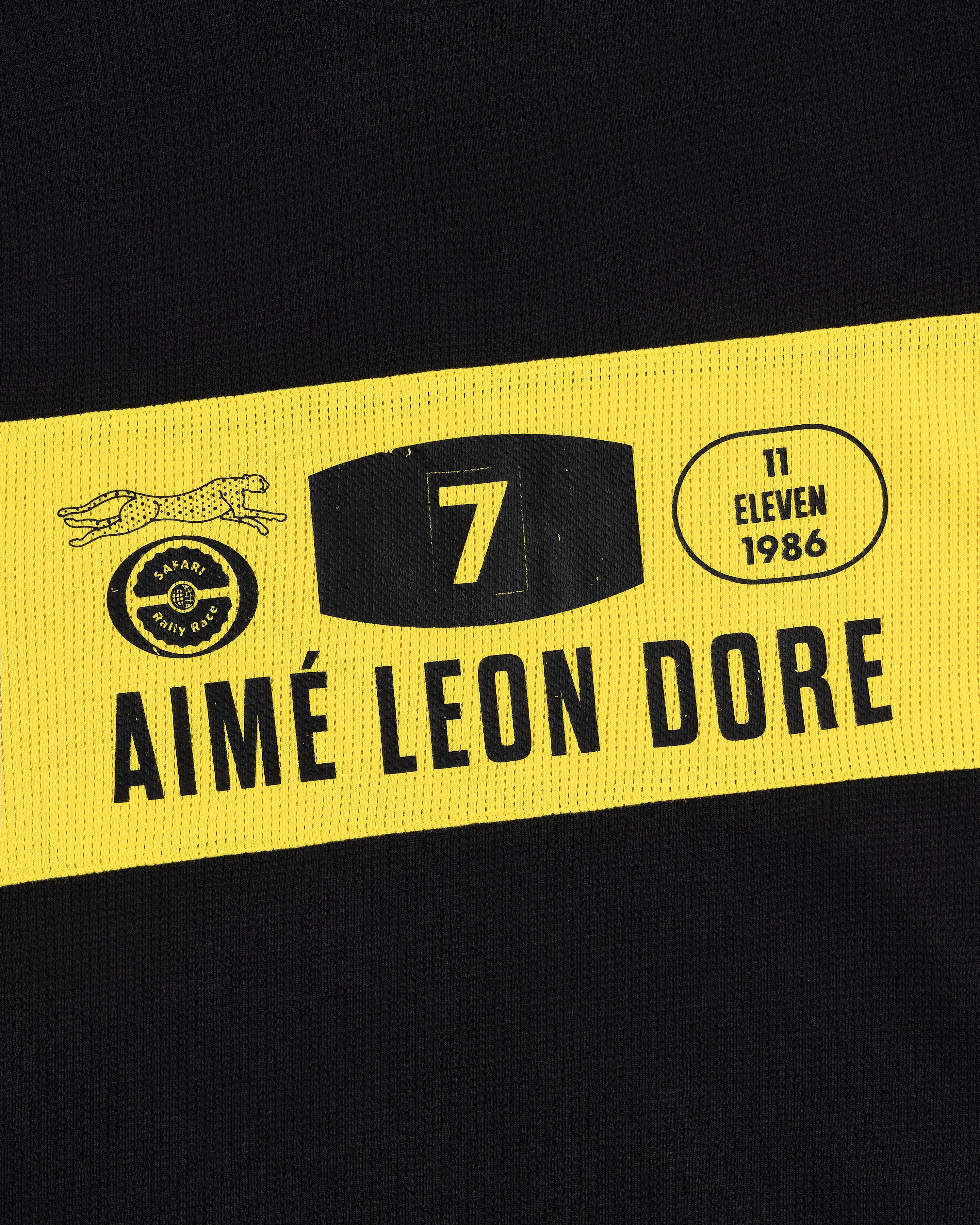 Close-up of the Long-Sleeve Rally Tee in black with a yellow stripe, AIMÉ LEON DORE logos, and the number 7.