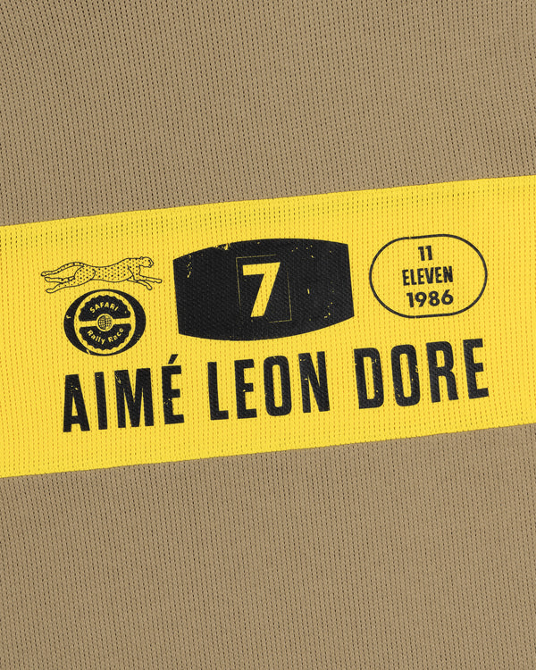 Long-Sleeve Rally Tee: yellow band with black text, AIMÉ LEON DORE, 7, and 11 ELEVEN 1986 on tan fabric.
