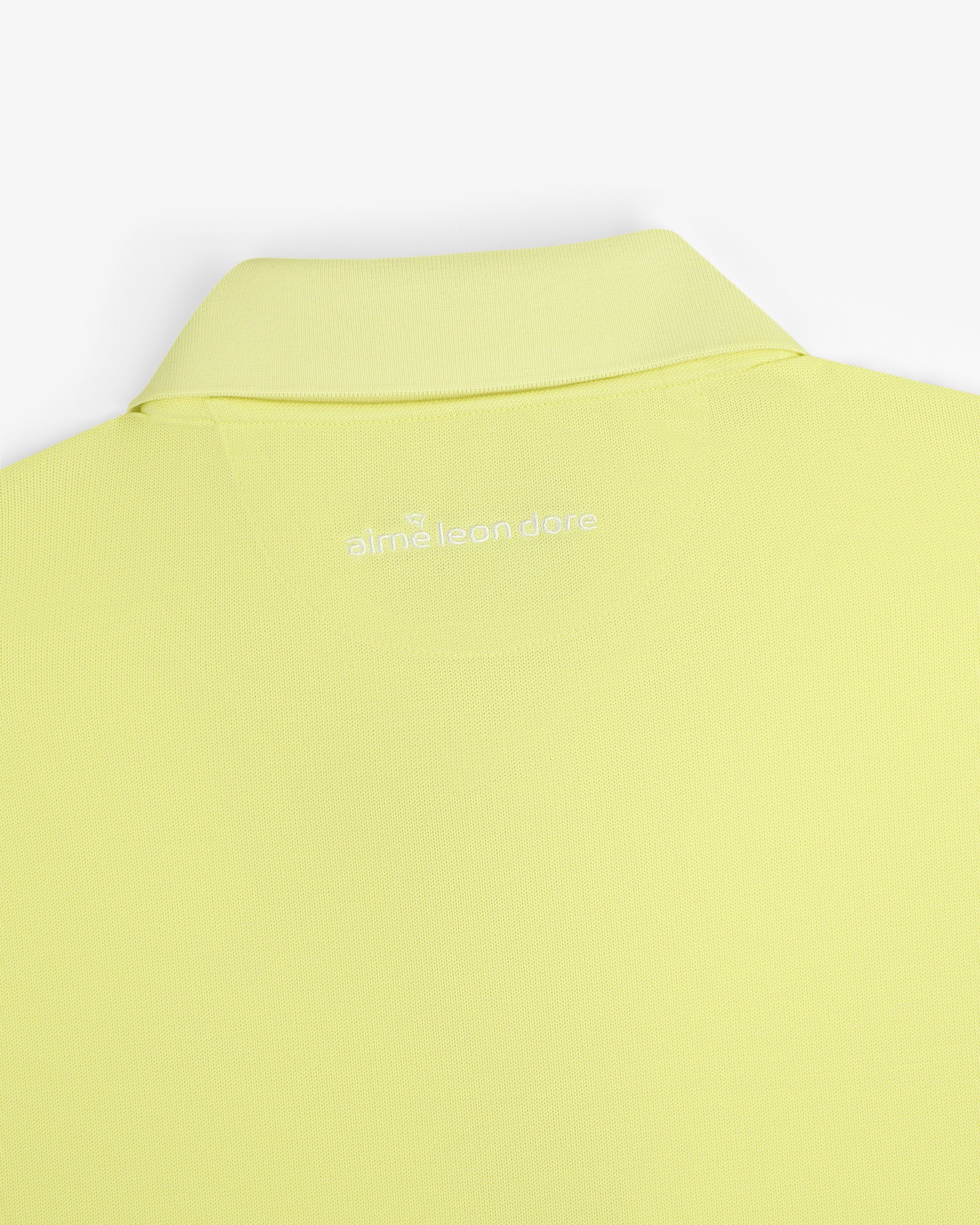A close-up of the back collar of the light yellow ALD Golf Polo with "alml éean done" printed in white.