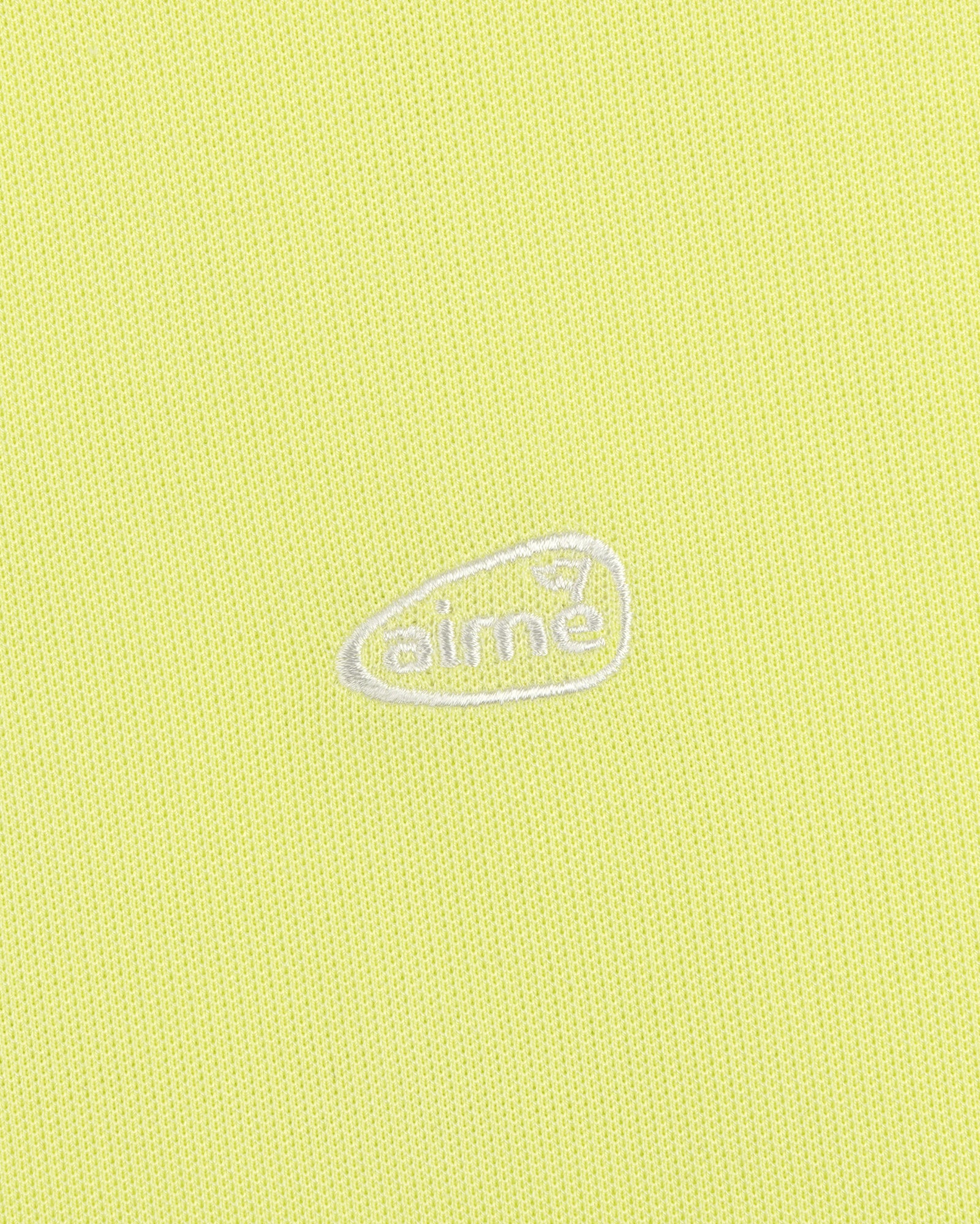 Light yellow ALD Golf Polo featuring textured fabric and an oval-shaped white aimé logo embroidered at the center.