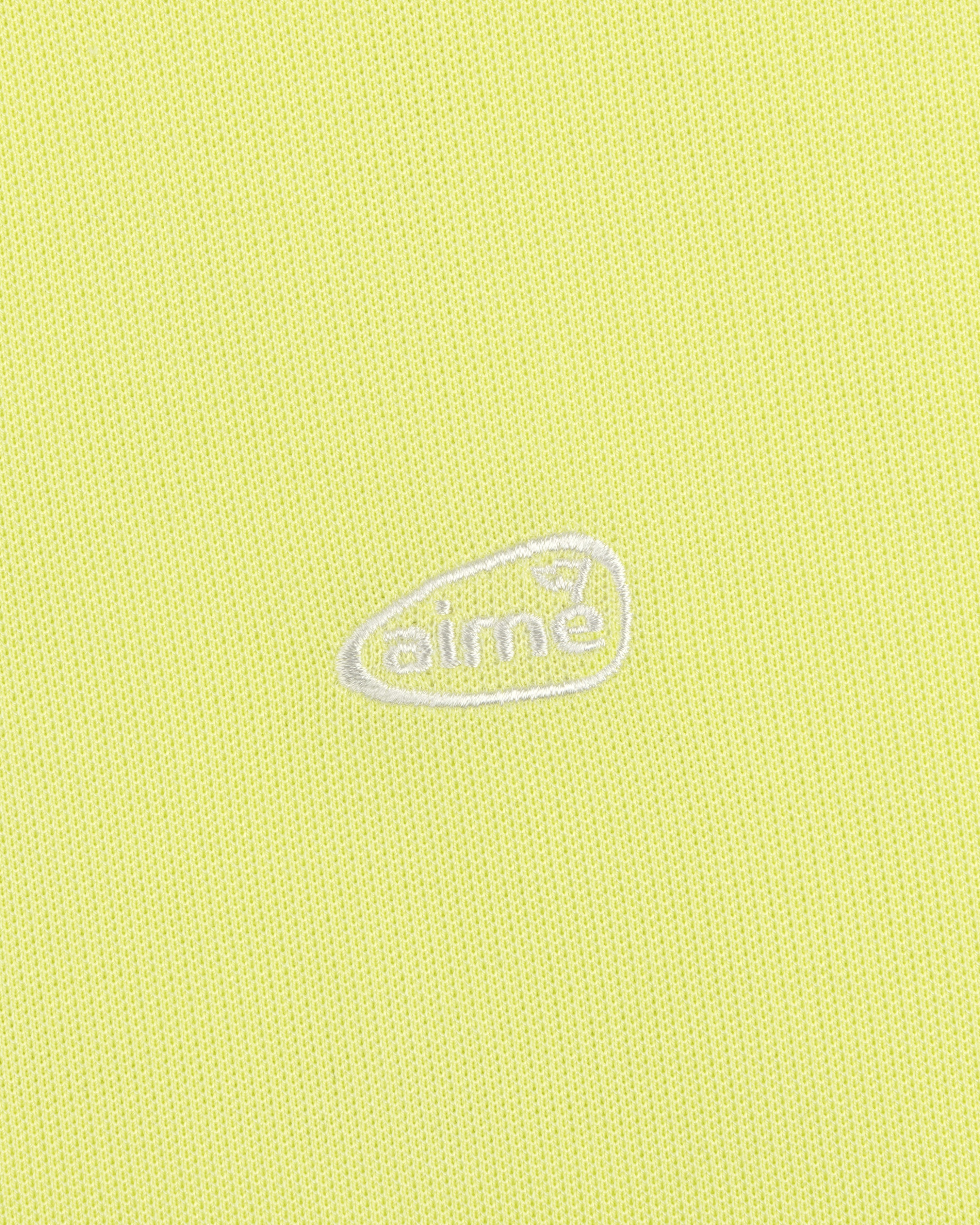Light yellow ALD Golf Polo featuring textured fabric and an oval-shaped white aimé logo embroidered at the center.