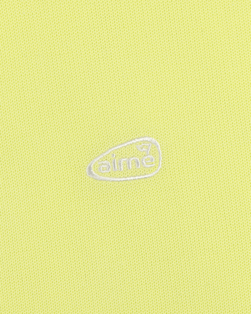 Light yellow ALD Golf Polo featuring textured fabric and an oval-shaped white aimé logo embroidered at the center.