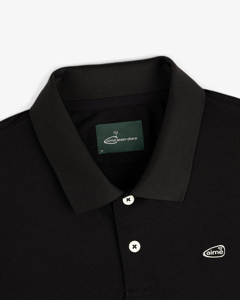 Close-up of the ALD Golf Polo, a black collared shirt with white buttons and a small Aimé Leon Dore chest logo patch.