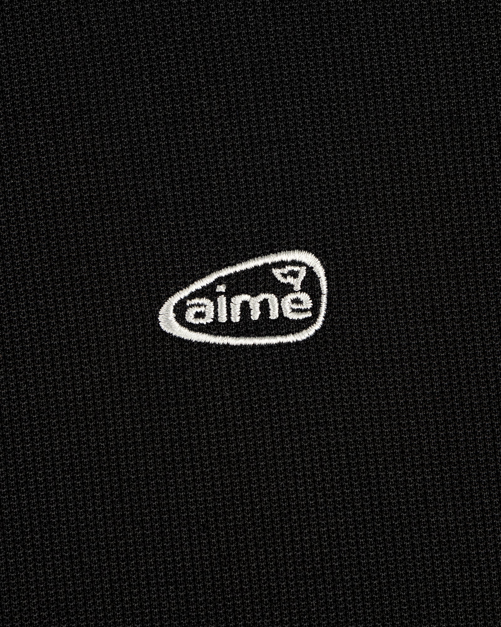 Black textured ALD Golf Polo with small white "aime" logo embroidered inside an irregular oval.