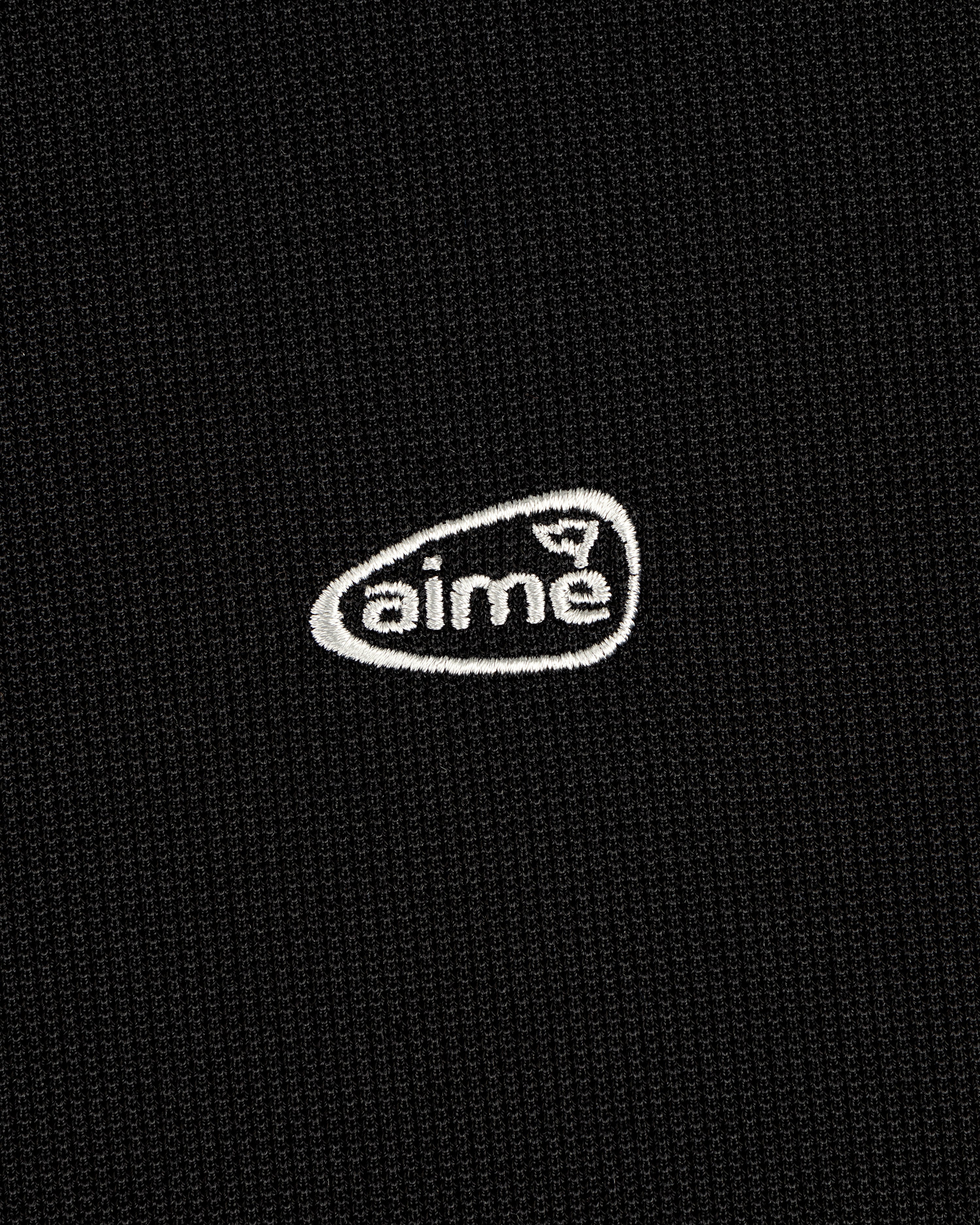 Black textured ALD Golf Polo with small white "aime" logo embroidered inside an irregular oval.