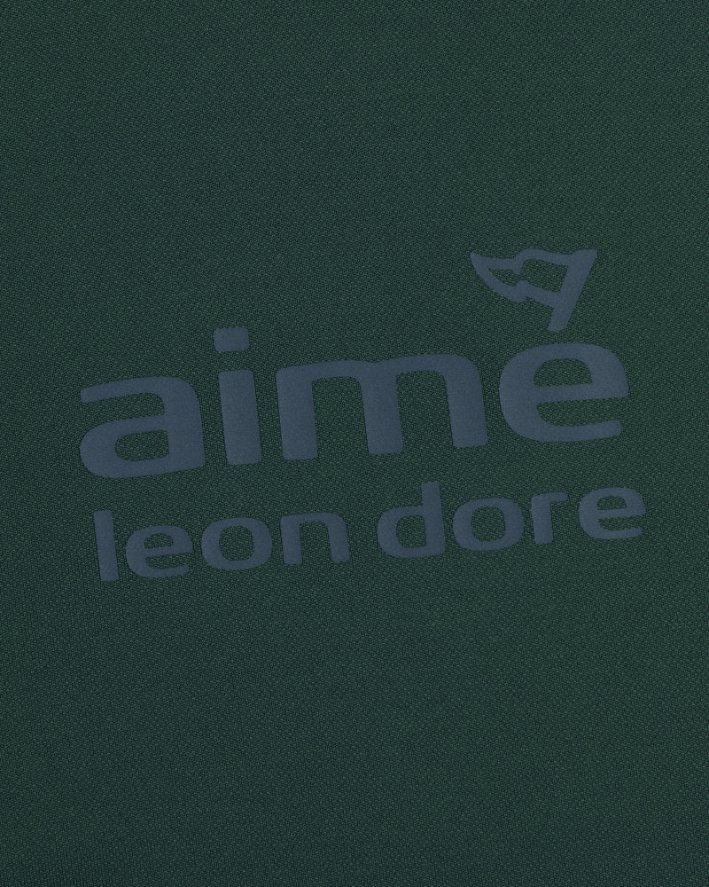 Close-up of the ALD Golf Tour Polo’s dark green fabric with bold aimé leon dore text and a flag graphic above the "e".
