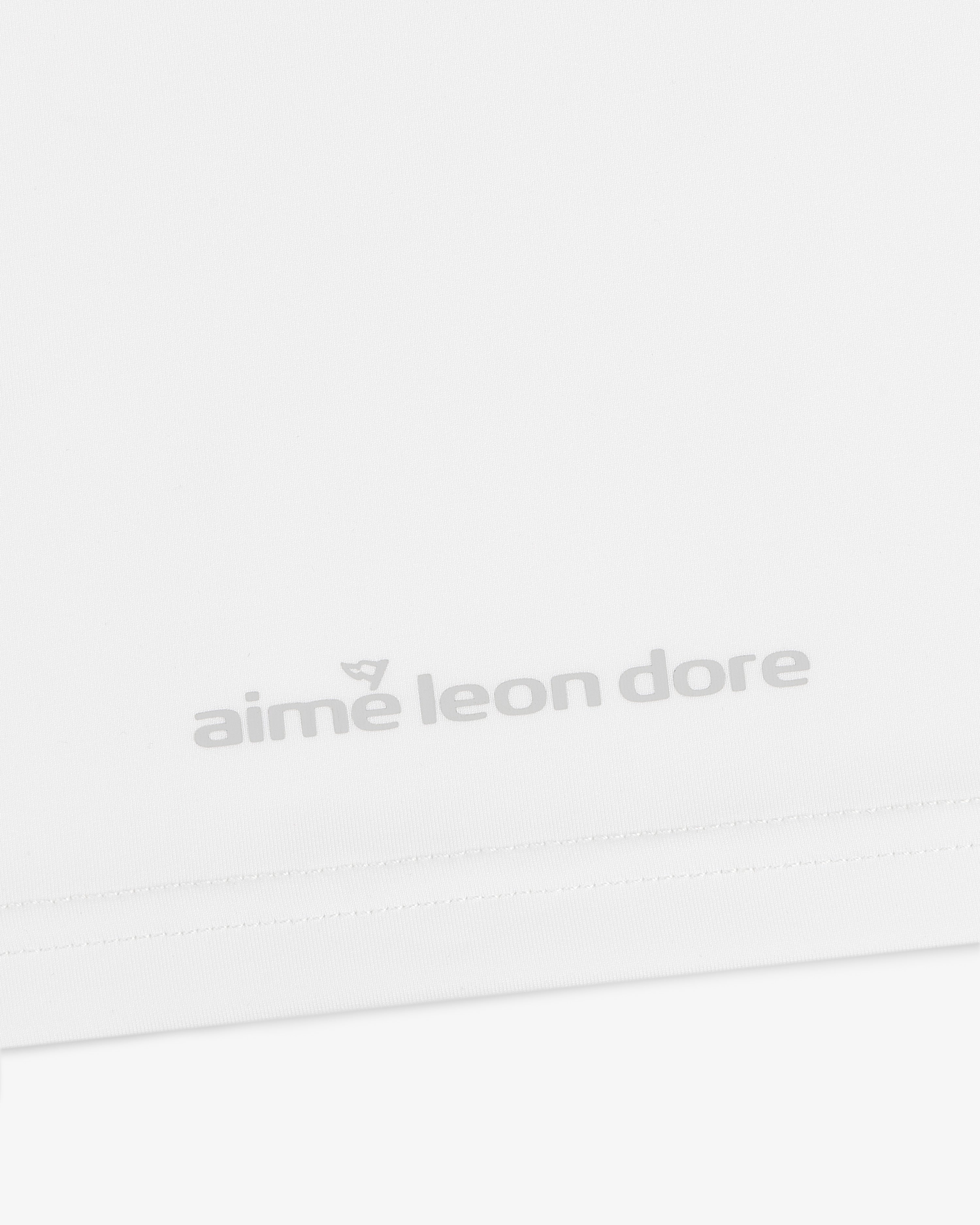 Close-up of a white ALD Golf Performance Tee with the aime leon dore logo in light gray near the bottom hem.
