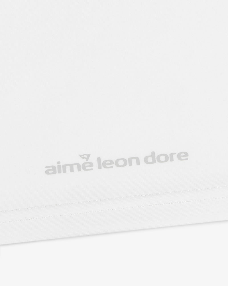 Close-up of a white ALD Golf Performance Tee with the aime leon dore logo in light gray near the bottom hem.