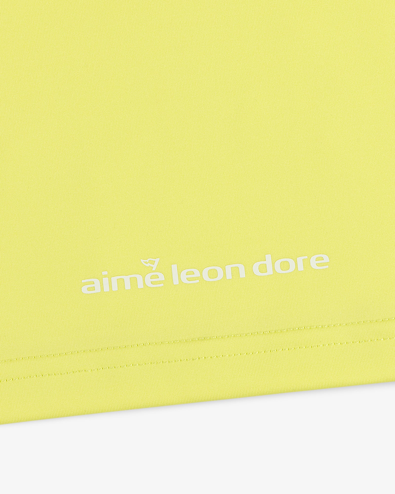 Close-up of the ALD Golf Performance Tee in yellow with the aime leon dore logo printed in white near the hem.