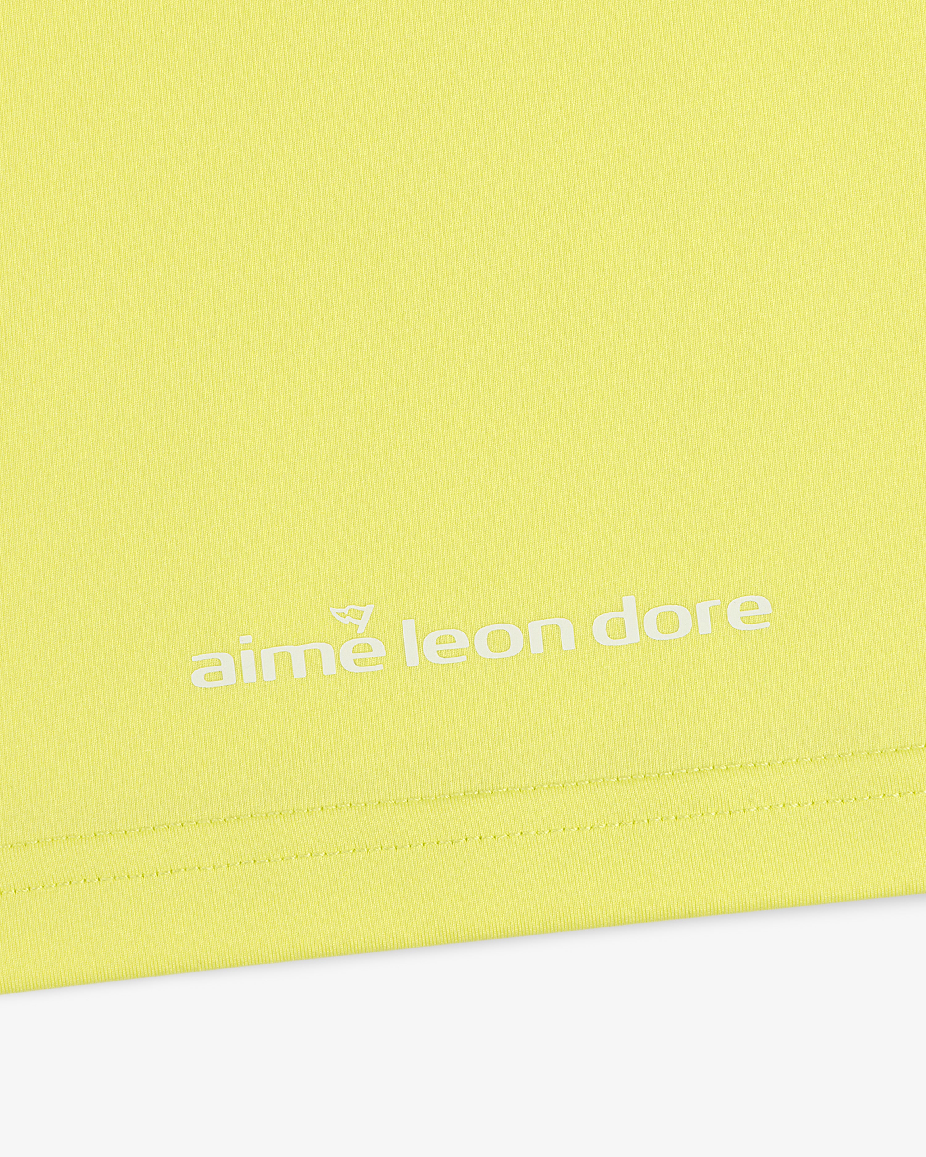 Close-up of the ALD Golf Performance Tee in yellow with the aime leon dore logo printed in white near the hem.