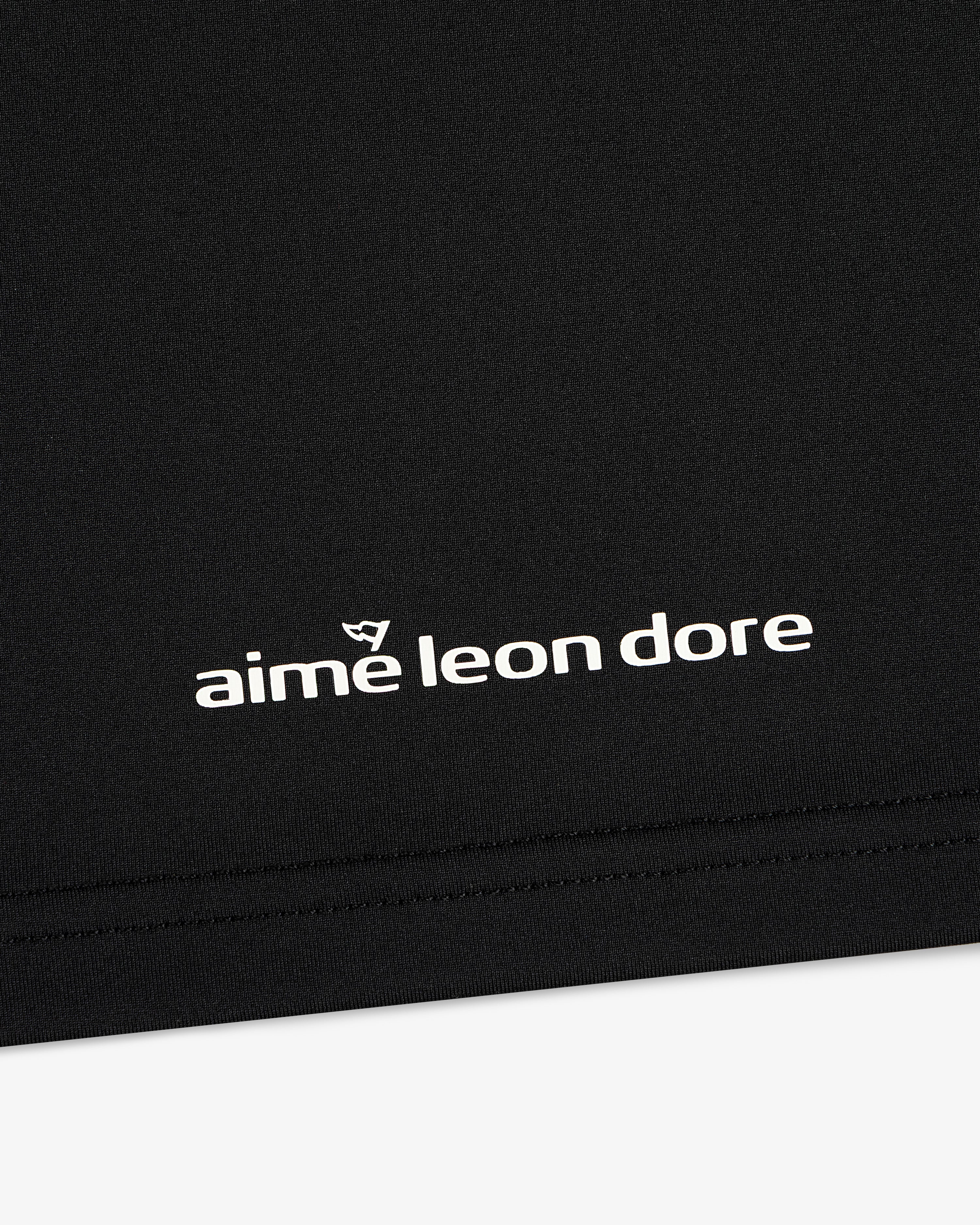 Close-up of black ALD Golf Performance Tee with white aime leon dore logo and stitching near the bottom edge.