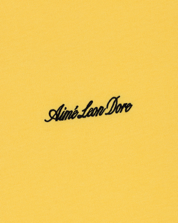 Black Aimé Leon Dore script logo embroidered on yellow Embroidered Logo Tee.