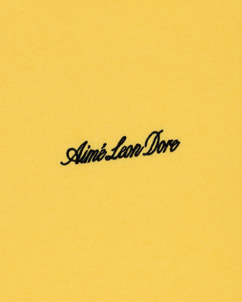 Black Aimé Leon Dore script logo embroidered on yellow Embroidered Logo Tee.