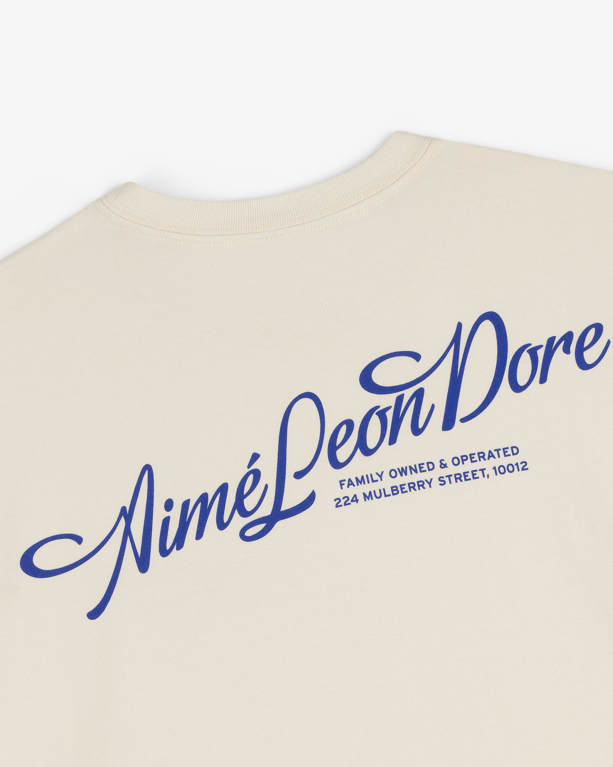 Pappoús Logo Tee: Beige shirt with large blue Aimé Leon Dore script and 224 Mulberry Street, 10012 on back.