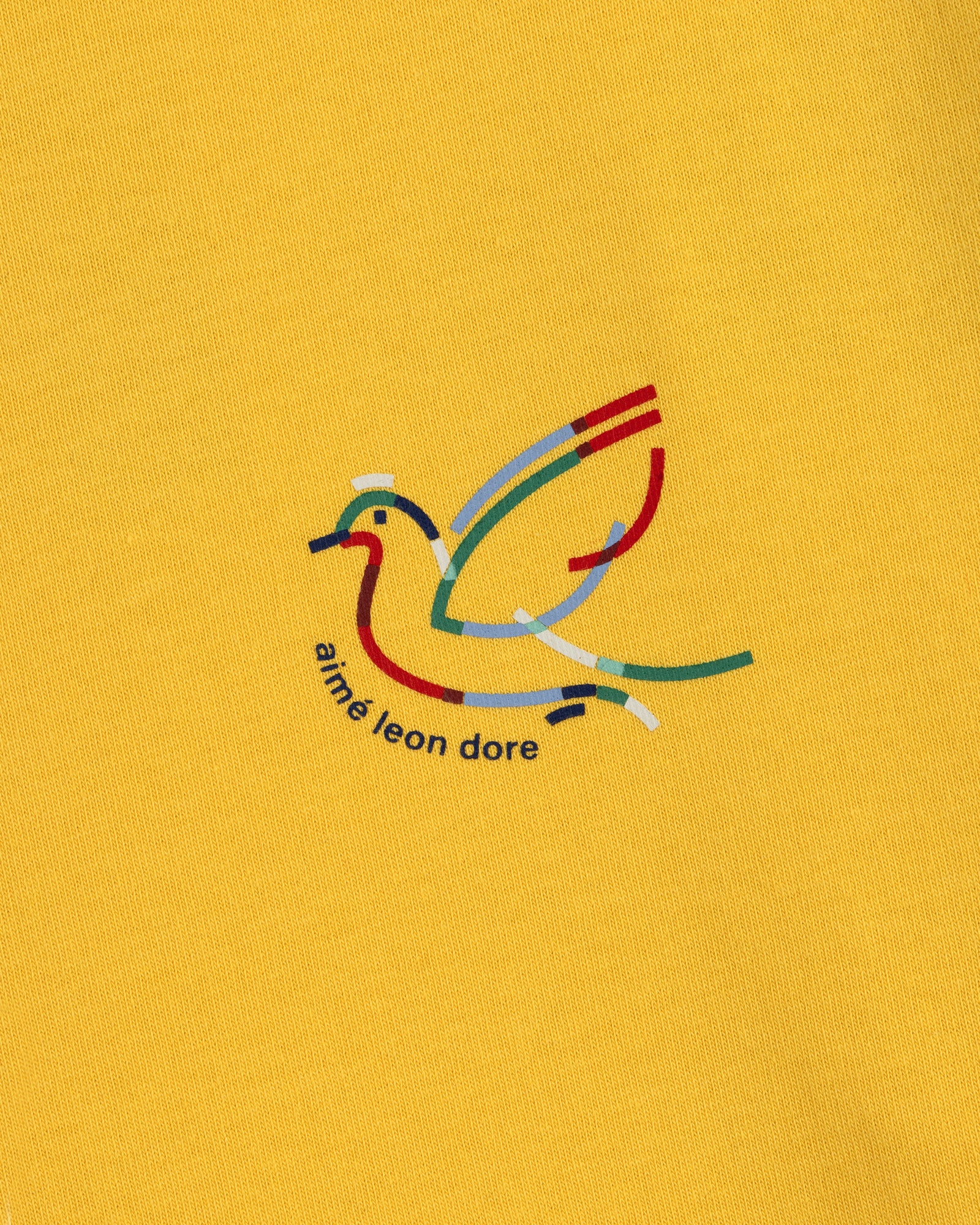 Yellow Long-Sleeve Souvenir Tee with a minimalist bird outline and "aimé leon dore" text beneath the design.