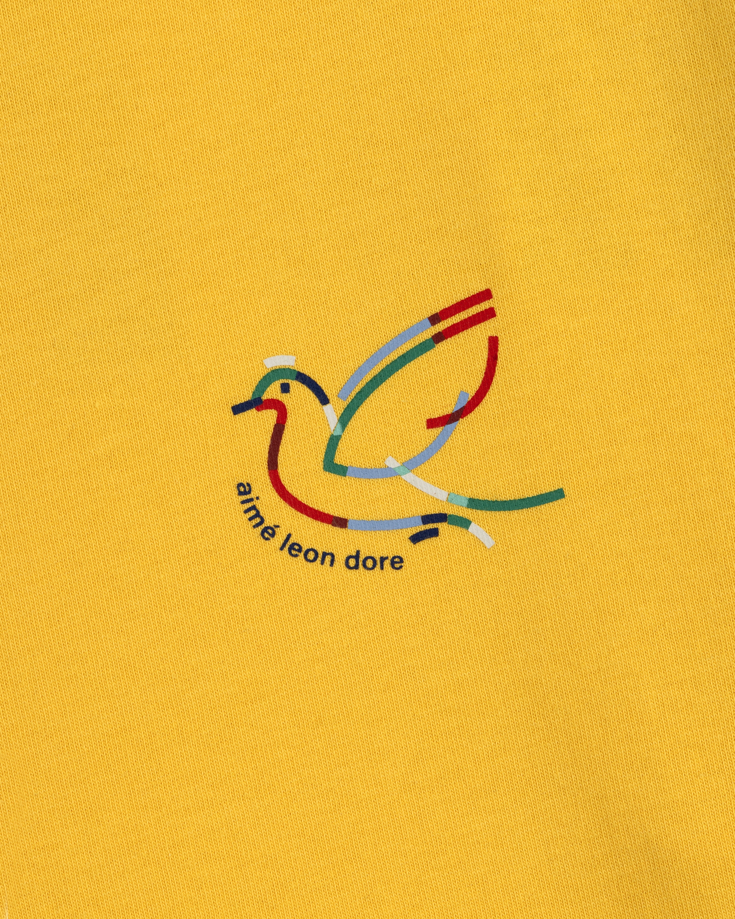 Yellow Long-Sleeve Souvenir Tee with a minimalist bird outline and "aimé leon dore" text beneath the design.