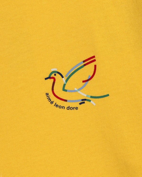 Yellow Long-Sleeve Souvenir Tee with a minimalist bird outline and "aimé leon dore" text beneath the design.