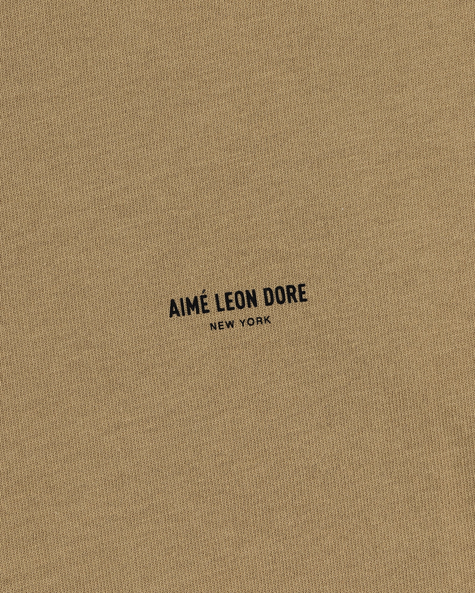 Close-up of tan Safari Tee with black AIMÉ LEON DORE NEW YORK text printed in the center.