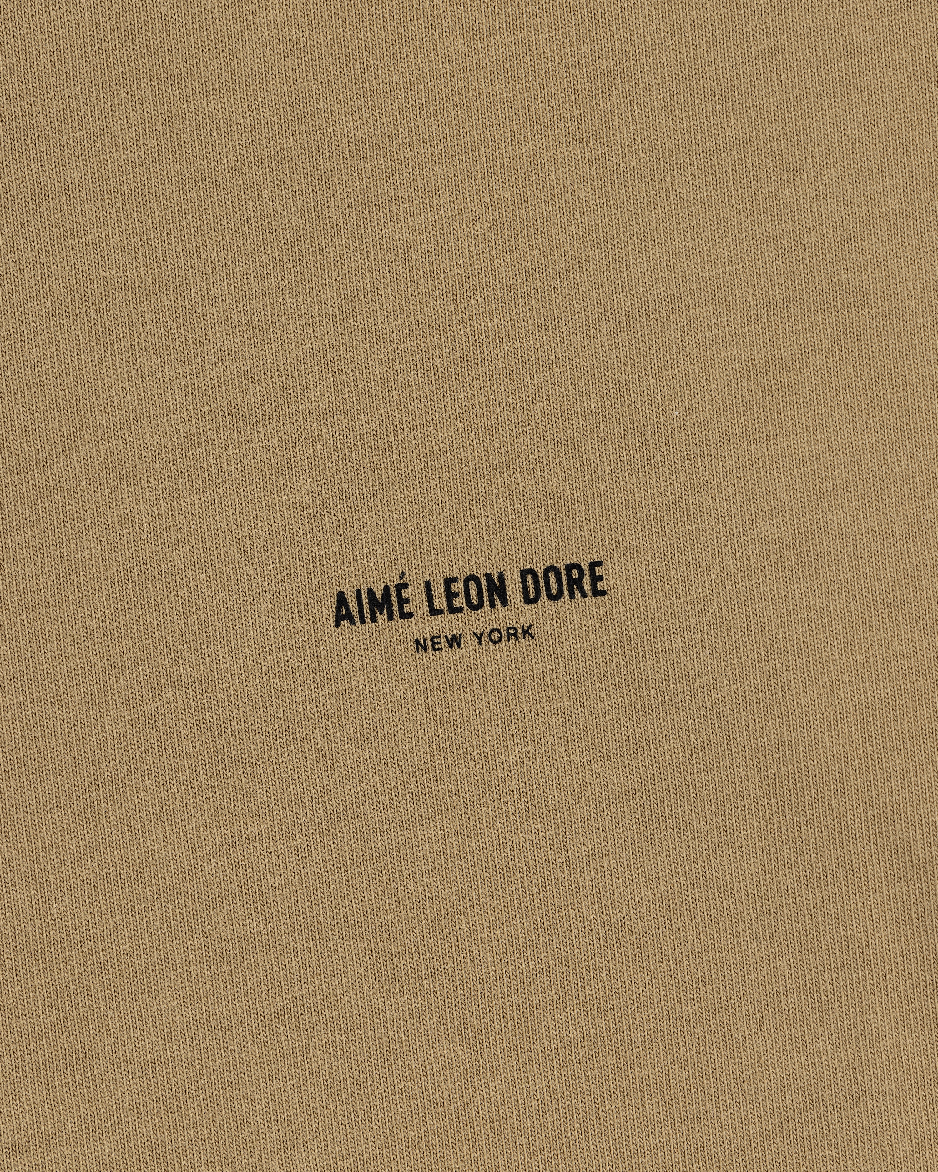 Close-up of tan Safari Tee with black AIMÉ LEON DORE NEW YORK text printed in the center.