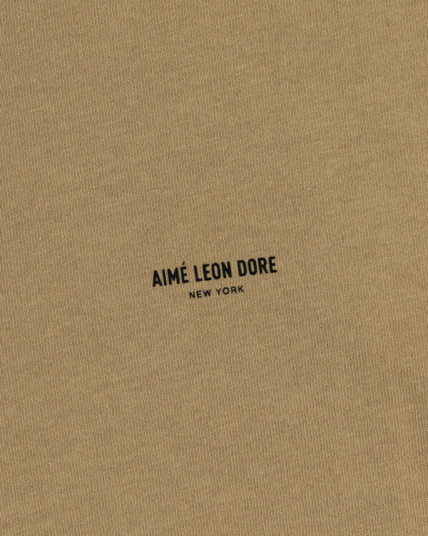 Close-up of tan Safari Tee with black AIMÉ LEON DORE NEW YORK text printed in the center.
