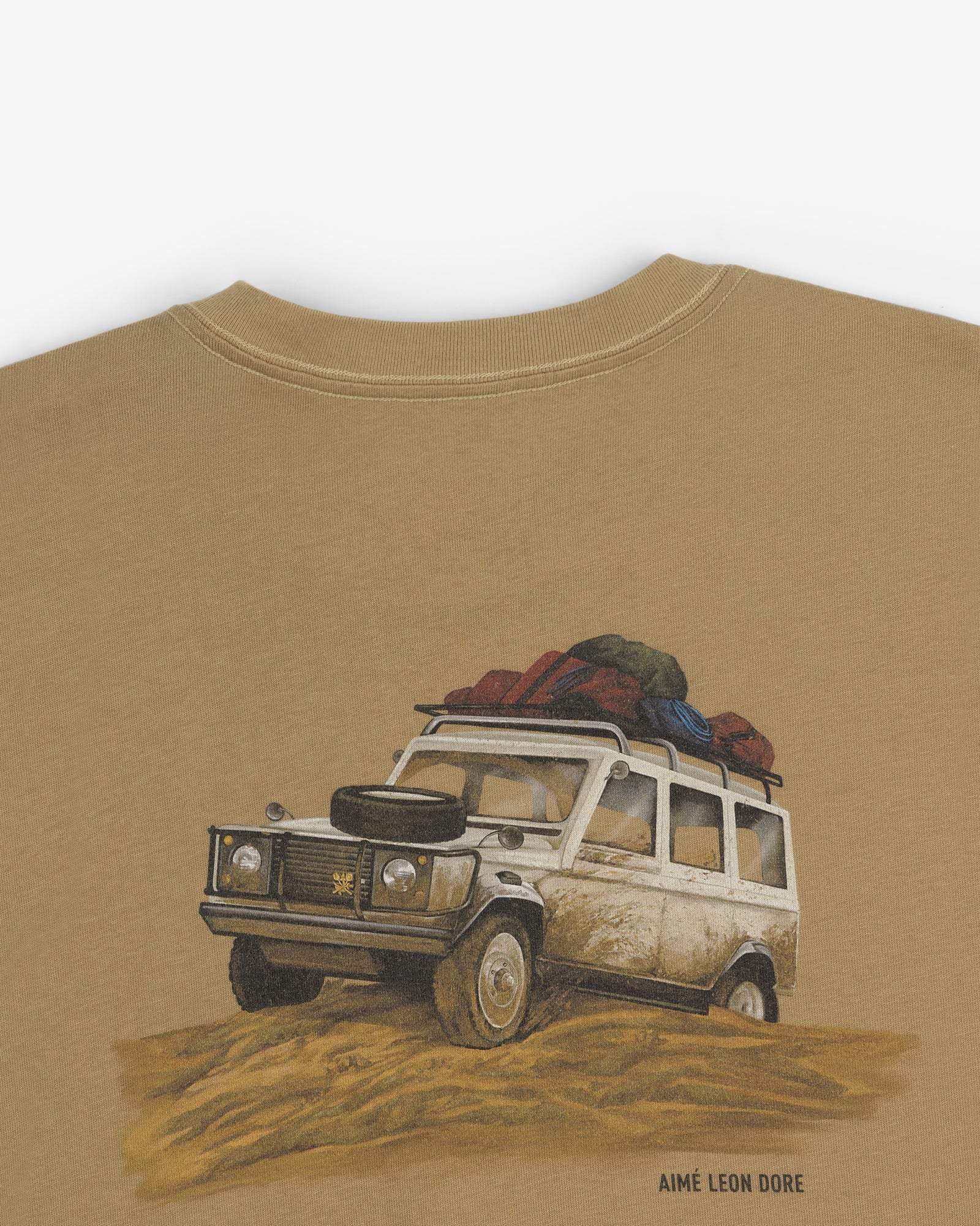 Safari Tee featuring a vintage off-road vehicle with luggage on top driving through sand; Aimé Leon Dore below.