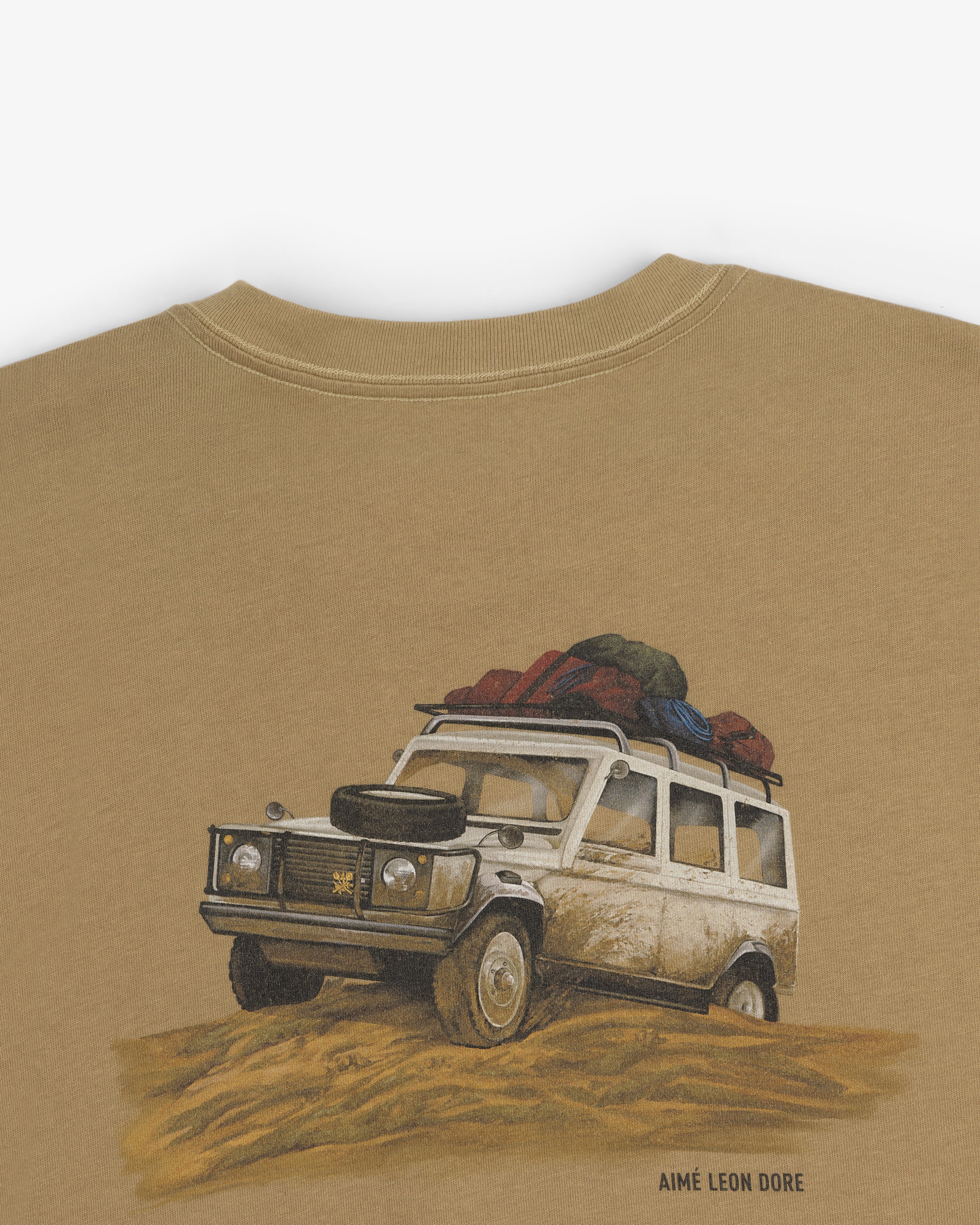 Safari Tee featuring a vintage off-road vehicle with luggage on top driving through sand; Aimé Leon Dore below.