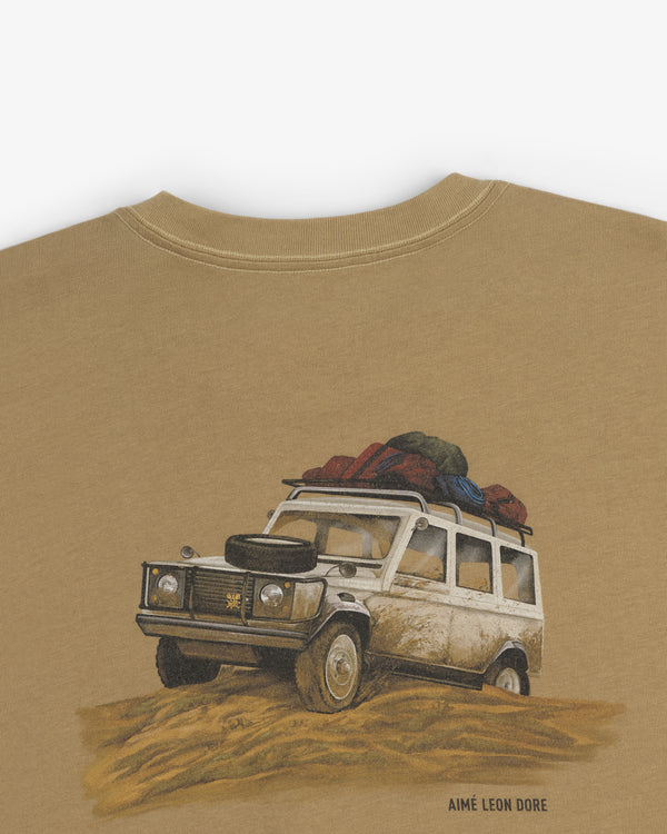 Safari Tee featuring a vintage off-road vehicle with luggage on top driving through sand; Aimé Leon Dore below.