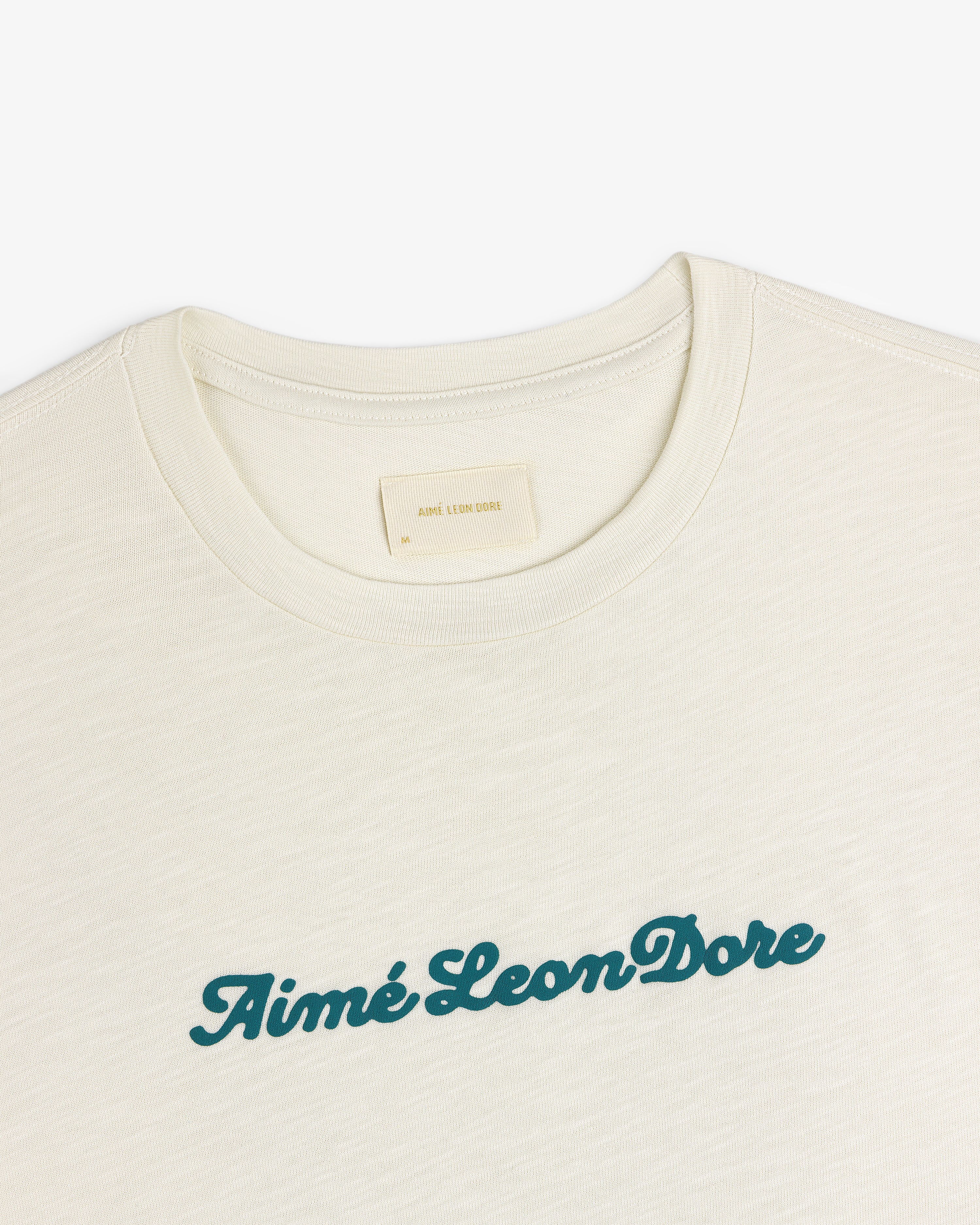 Cream Puff Print Slub Logo Tee with Aimé Leon Dore in green script across the chest.