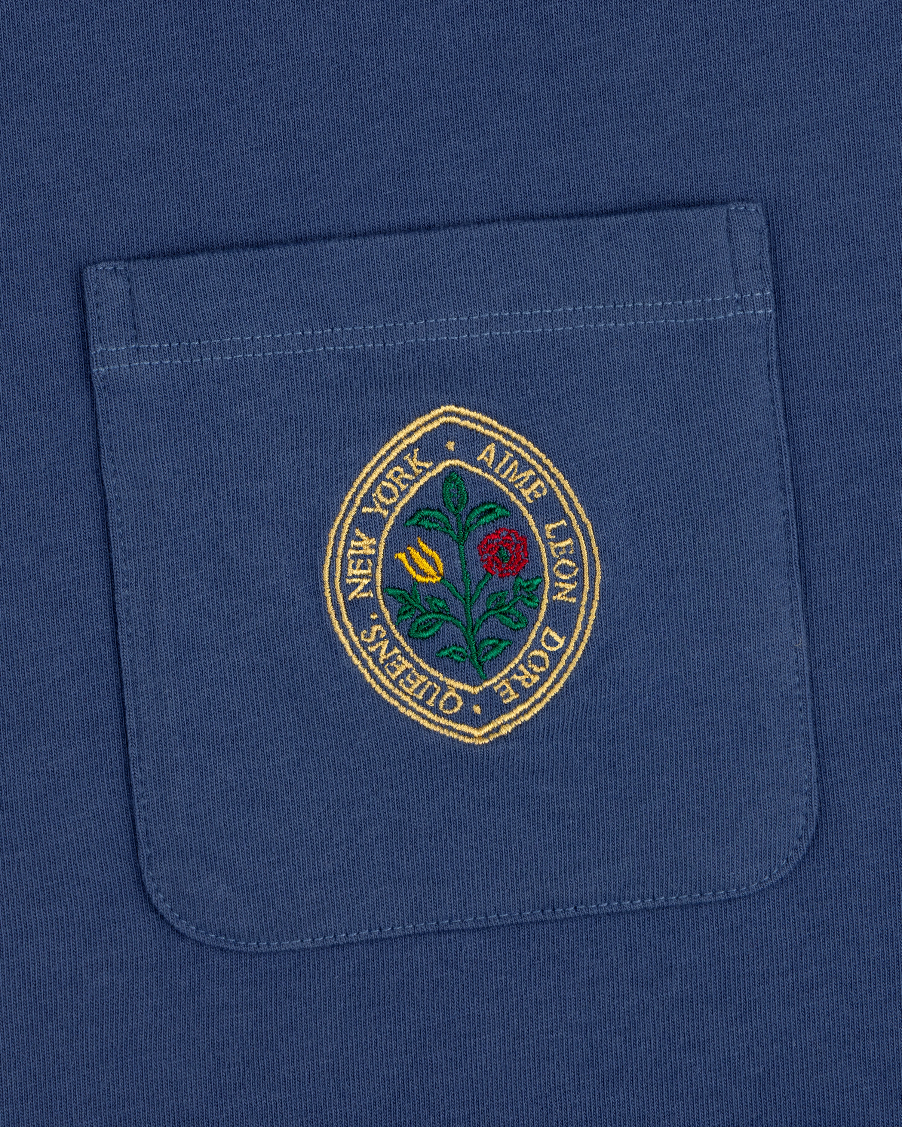 Botanical Crest Pocket Tee: blue shirt pocket with a circular floral patch and "New York - Ames Leon Dore - Queens.