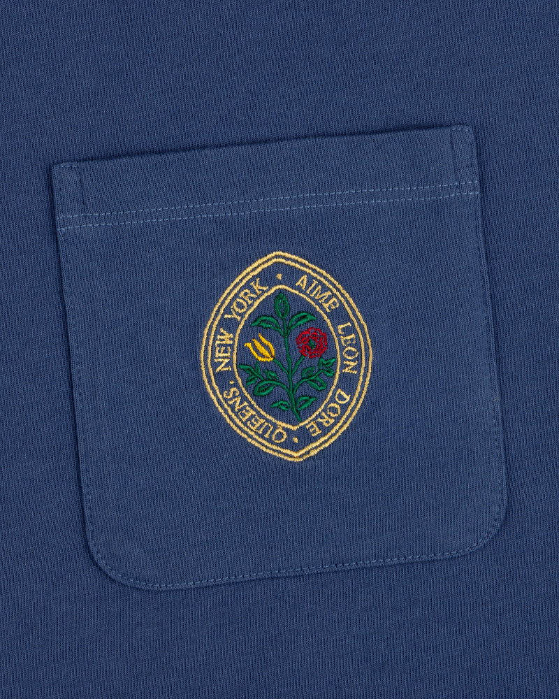 Botanical Crest Pocket Tee: blue shirt pocket with a circular floral patch and "New York - Ames Leon Dore - Queens.
