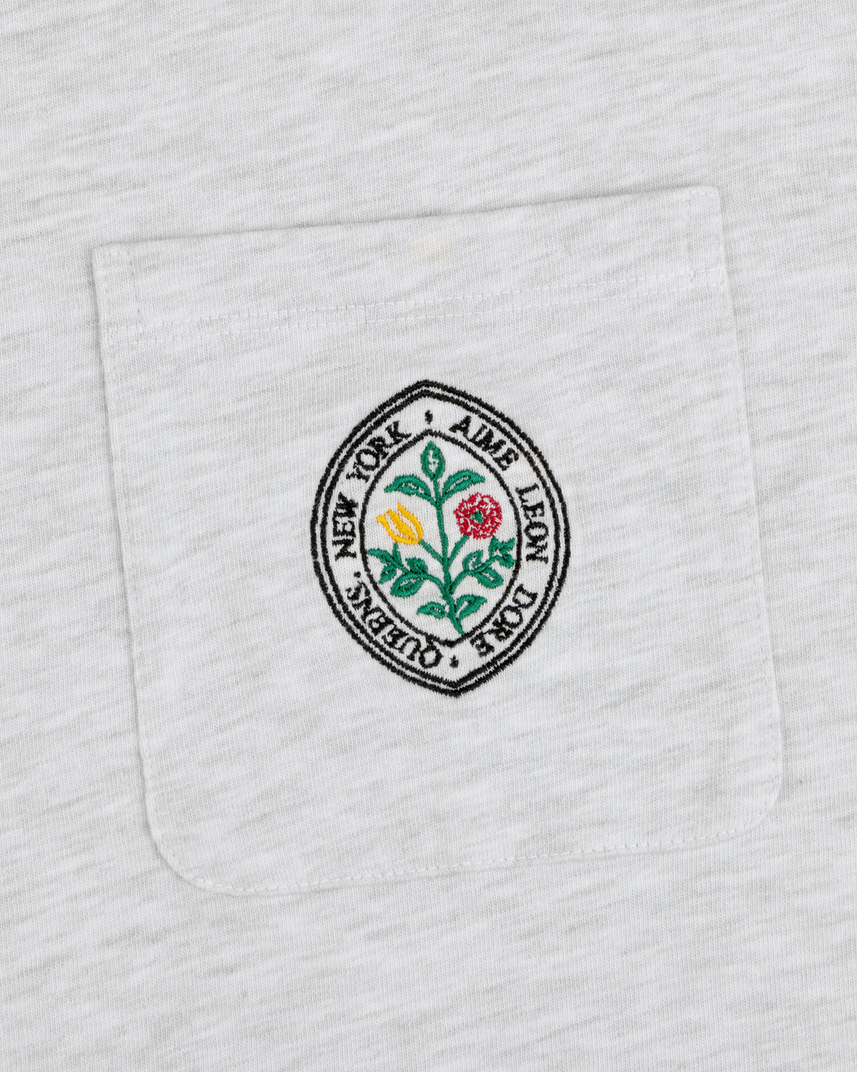 White pocket tee with round floral patch and text: Botanical Crest Pocket Tee by Aime Leon Dore New York Queens.