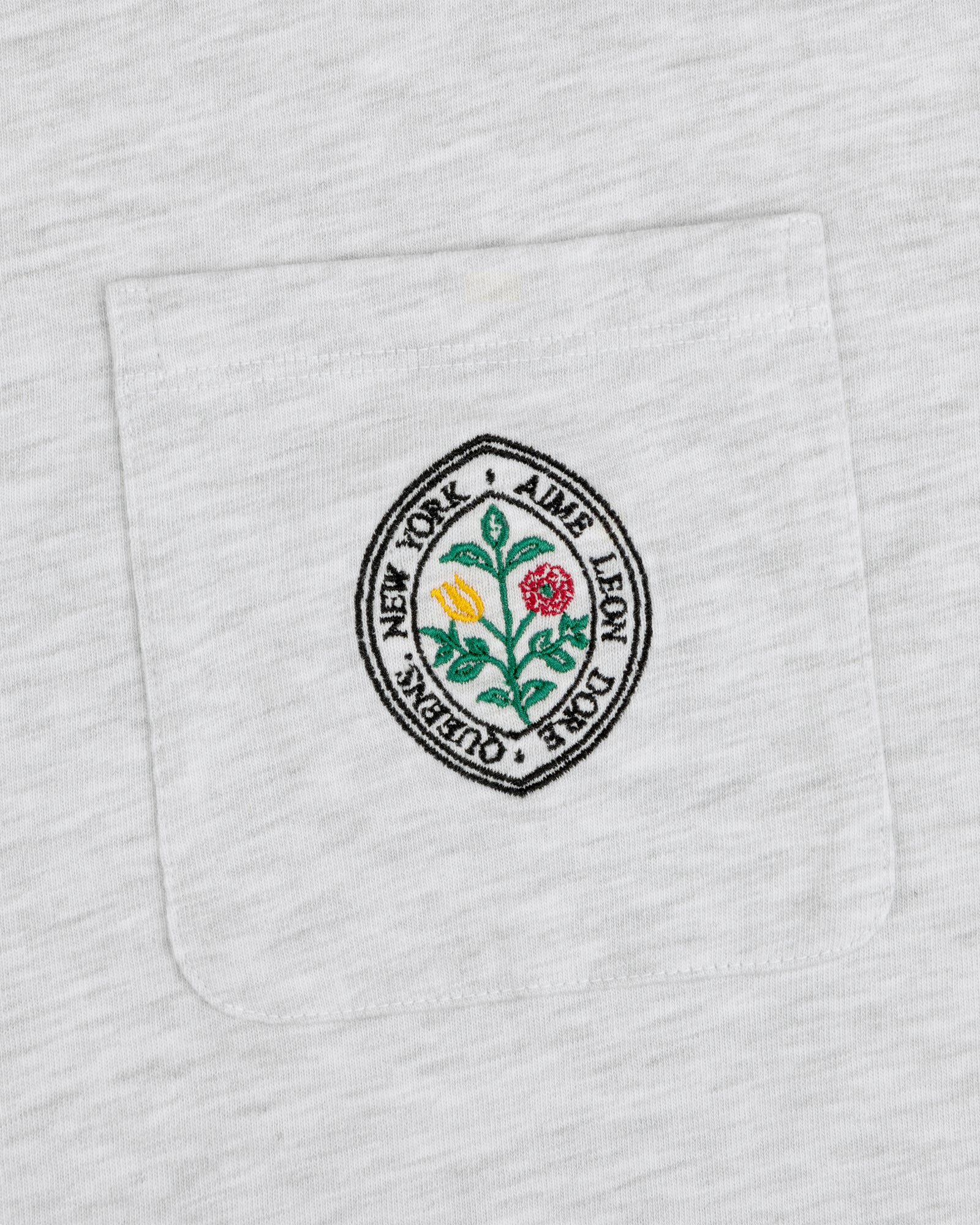 White pocket tee with round floral patch and text: Botanical Crest Pocket Tee by Aime Leon Dore New York Queens.