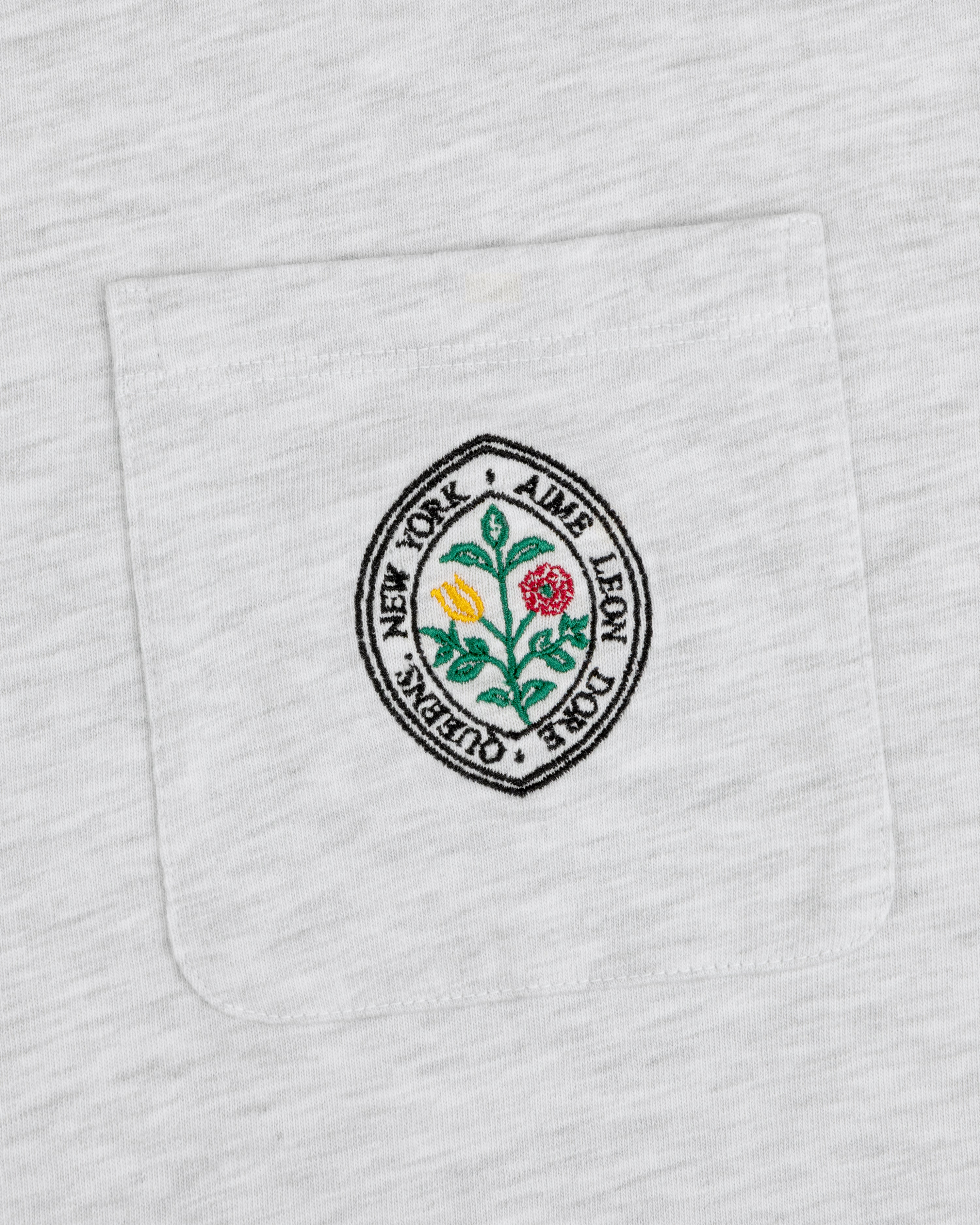 White pocket tee with round floral patch and text: Botanical Crest Pocket Tee by Aime Leon Dore New York Queens.