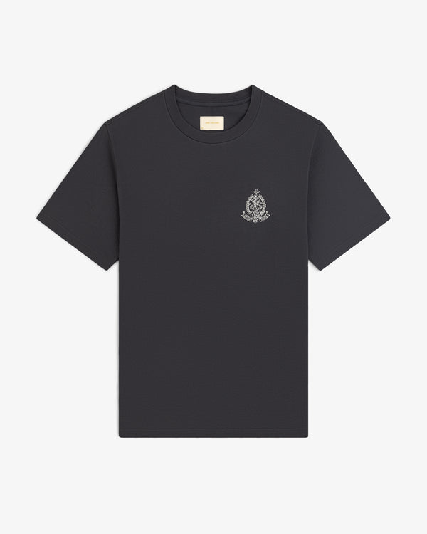 Saint George Graphic Tee—black short-sleeve shirt with a small ornate white crest on the left chest, shown on white.