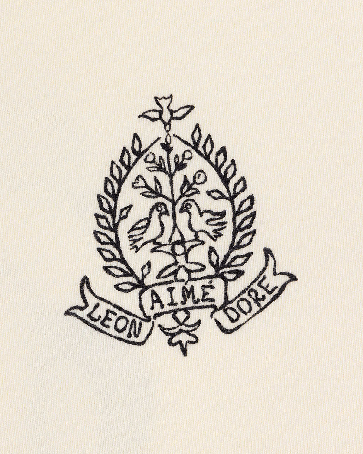 Black line art of two birds on branches in a laurel wreath, with LEON and DORE banners, on the Saint George Graphic Tee.