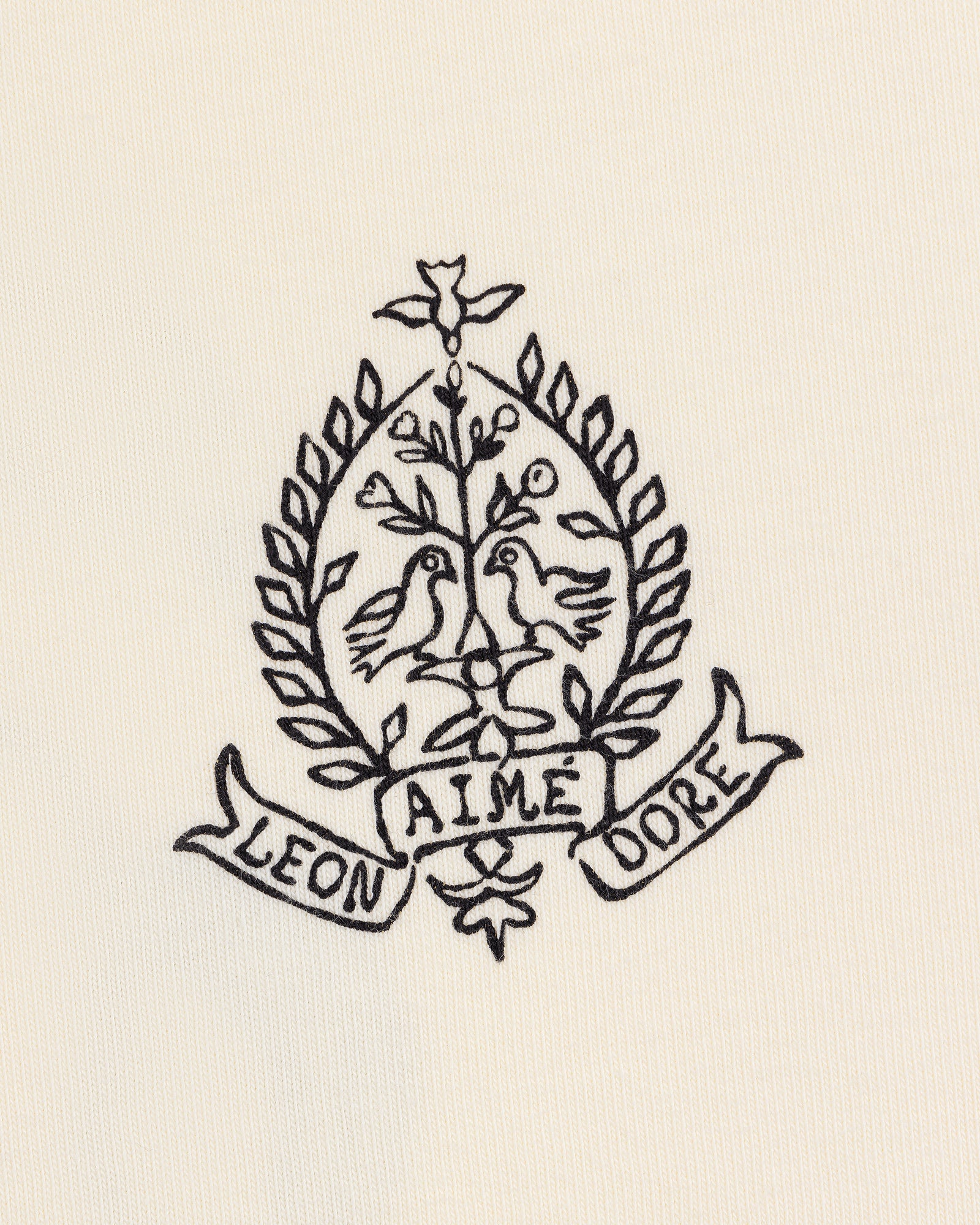 Black line art of two birds on branches in a laurel wreath, with LEON and DORE banners, on the Saint George Graphic Tee.