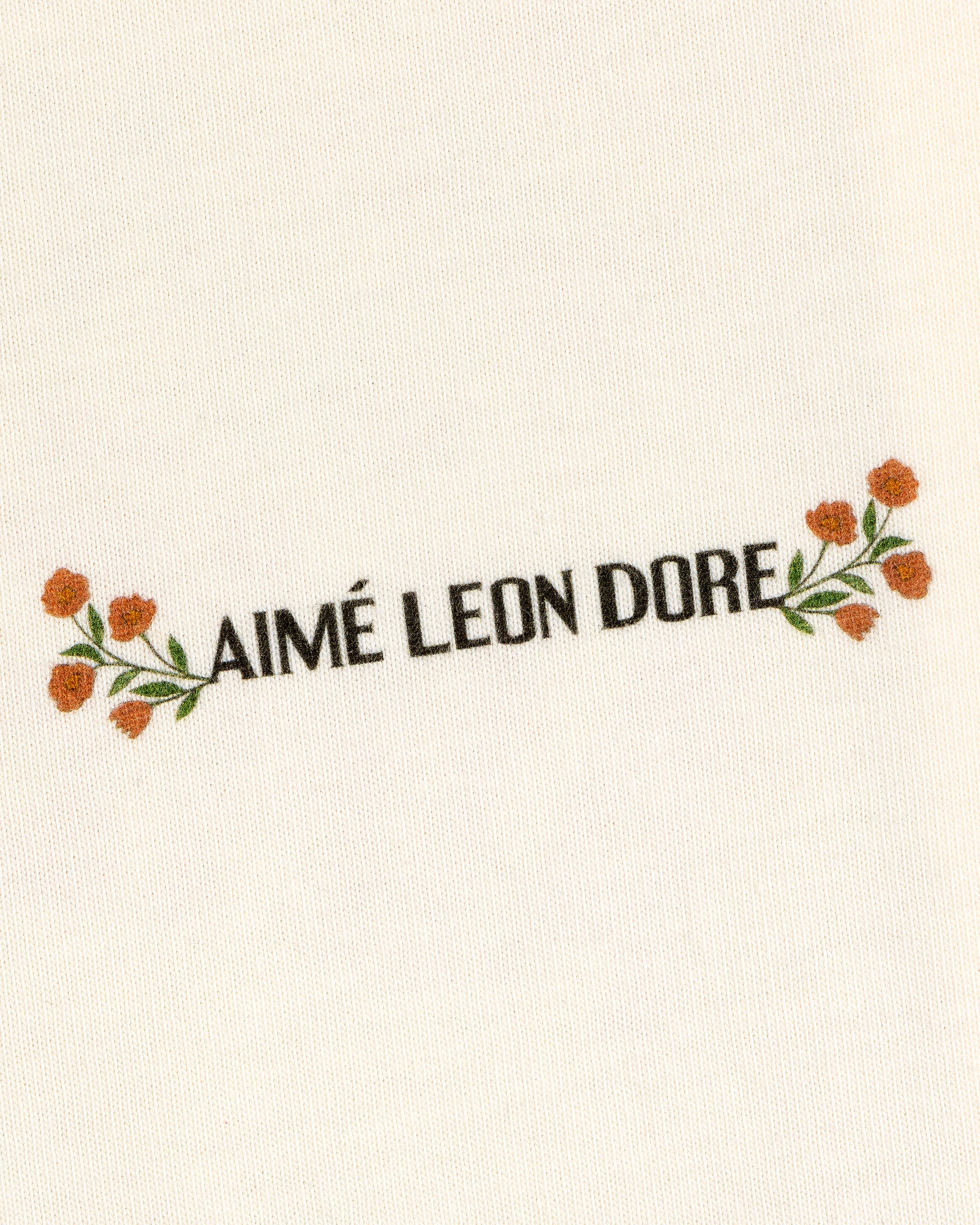 White Aimé Postcard Tee featuring black AIMÉ LEON DORE text, with orange flowers and green leaves.