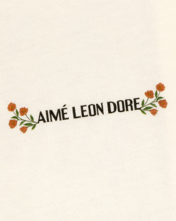 White Aimé Postcard Tee featuring black AIMÉ LEON DORE text, with orange flowers and green leaves.