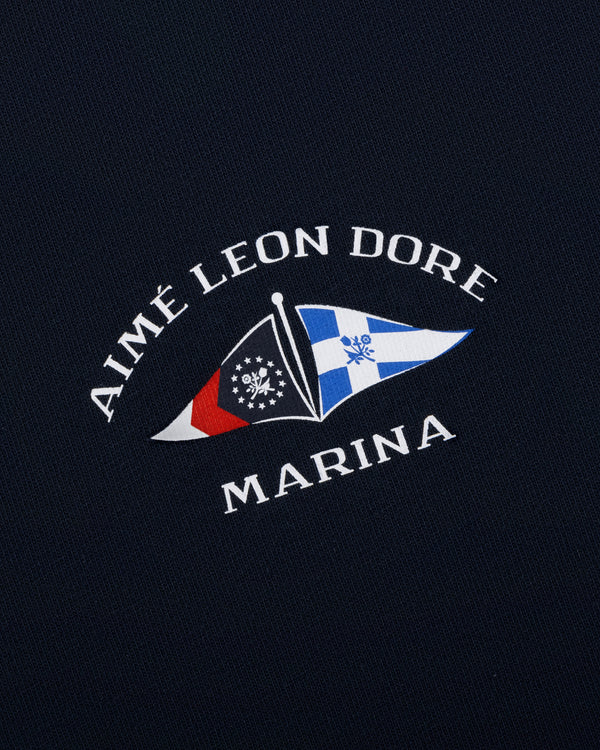 Navy Marina Tee featuring AIMÉ LEON DORE MARINA text and two nautical flags in the center.