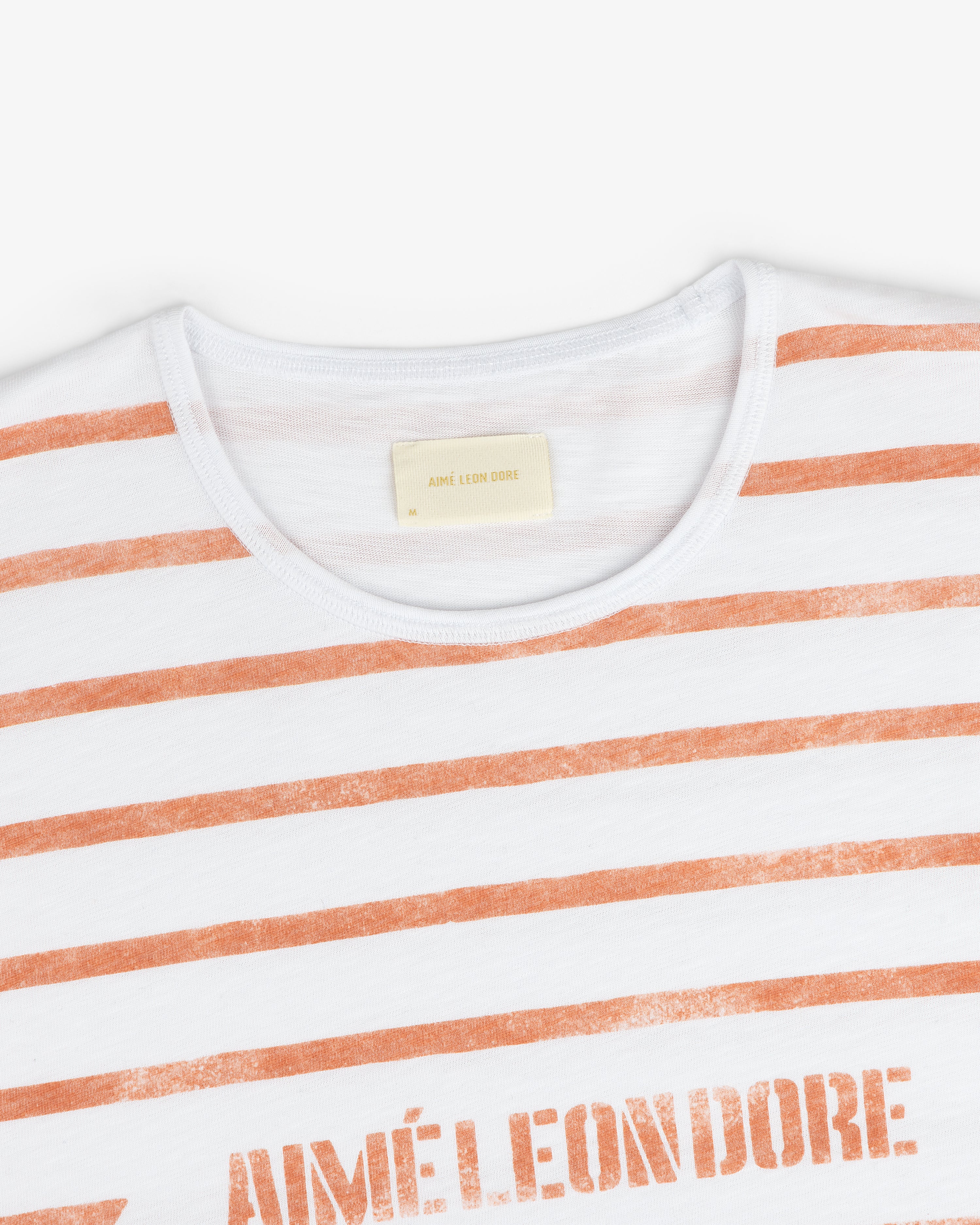 Slub Beach Tee: White t-shirt with orange stripes and AIMÉ LEON DORE printed on the chest.
