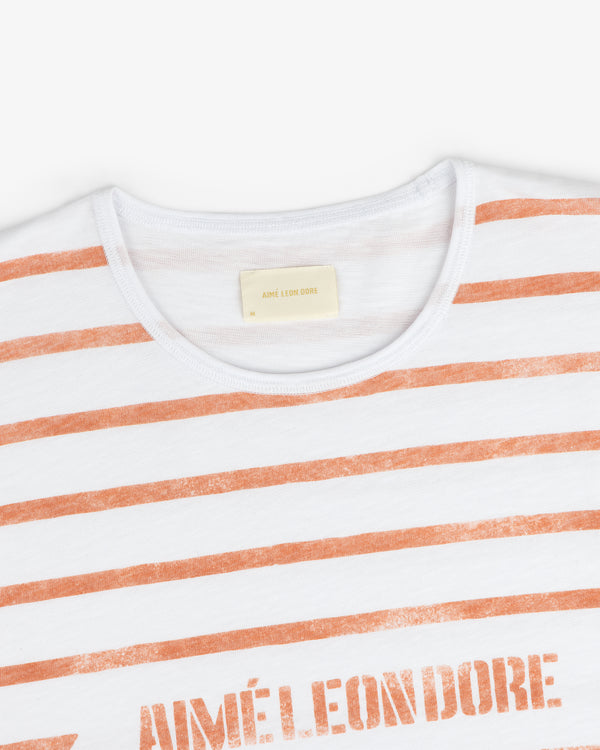 Slub Beach Tee: White t-shirt with orange stripes and AIMÉ LEON DORE printed on the chest.
