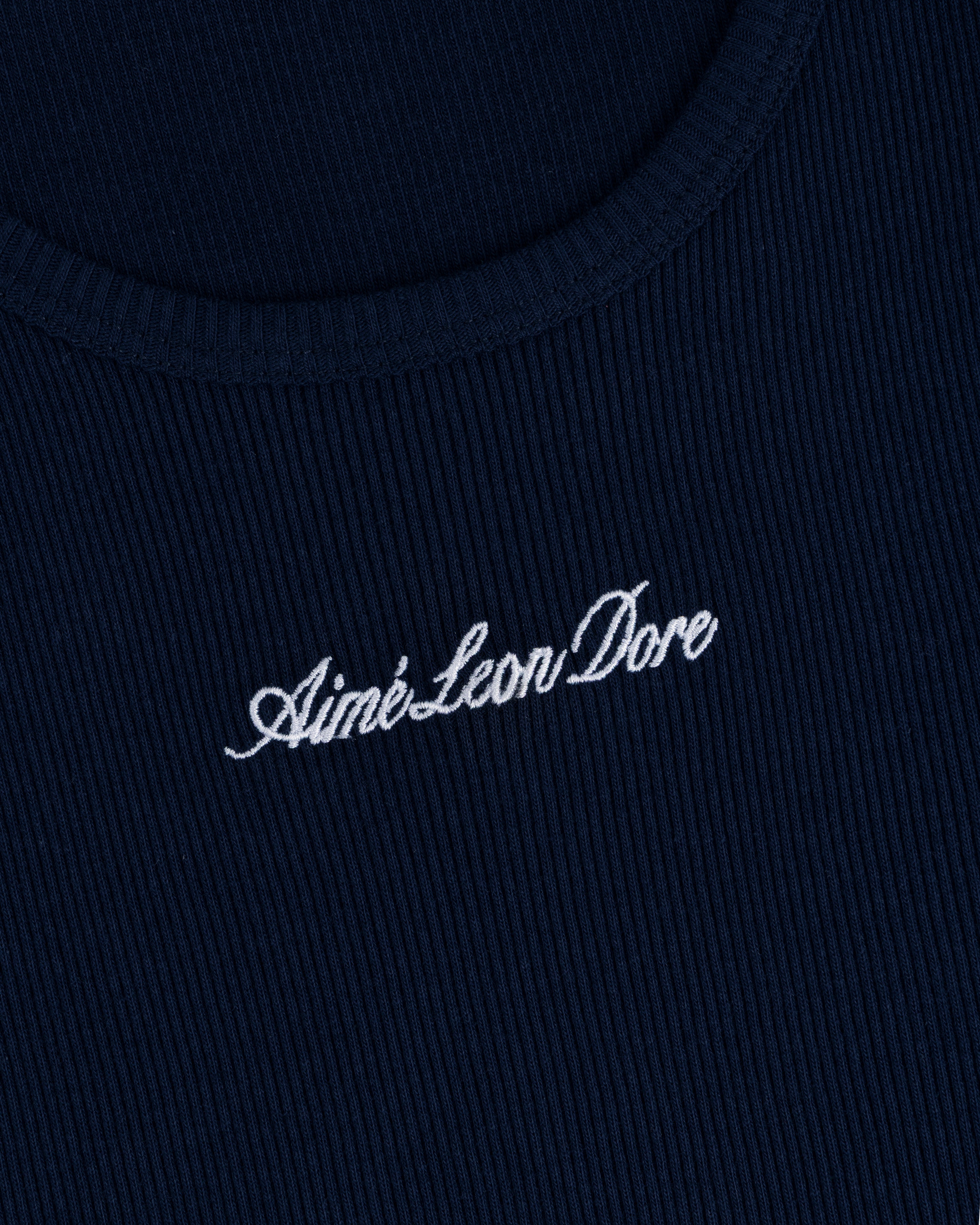 Close-up of navy ribbed fabric on the Embroidered Logo Tank Top with Aimé Leon Dore in white cursive.