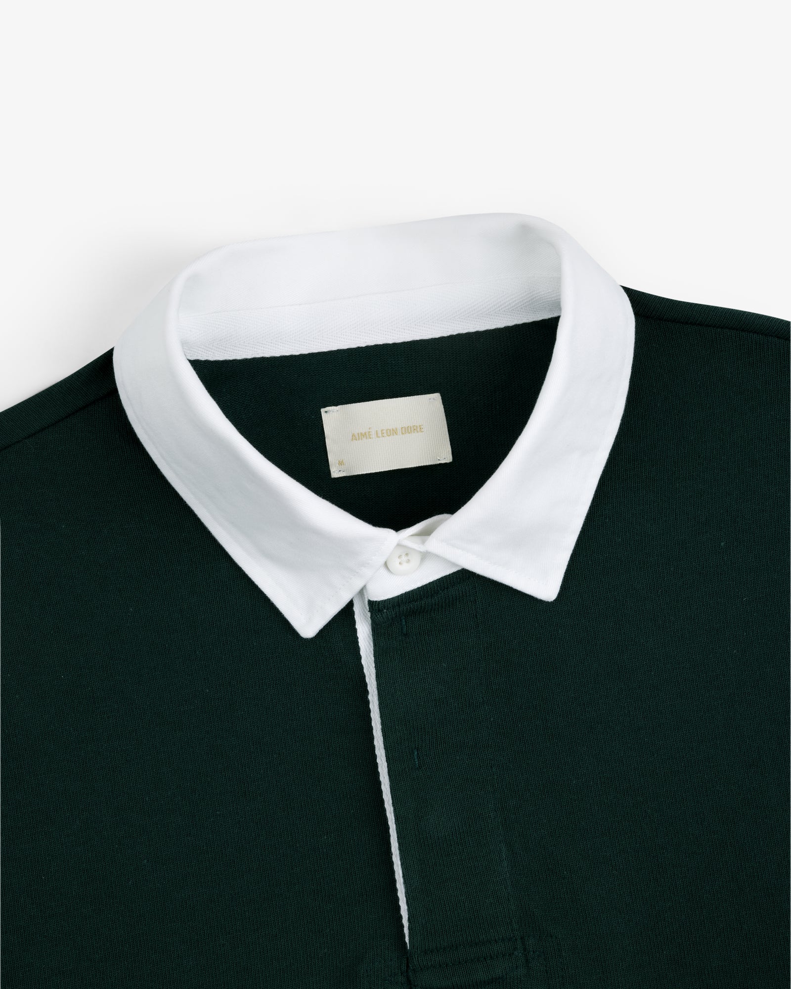 Script Paneled Rugby in dark green with a white collar and visible neckline label, shown on a plain background.