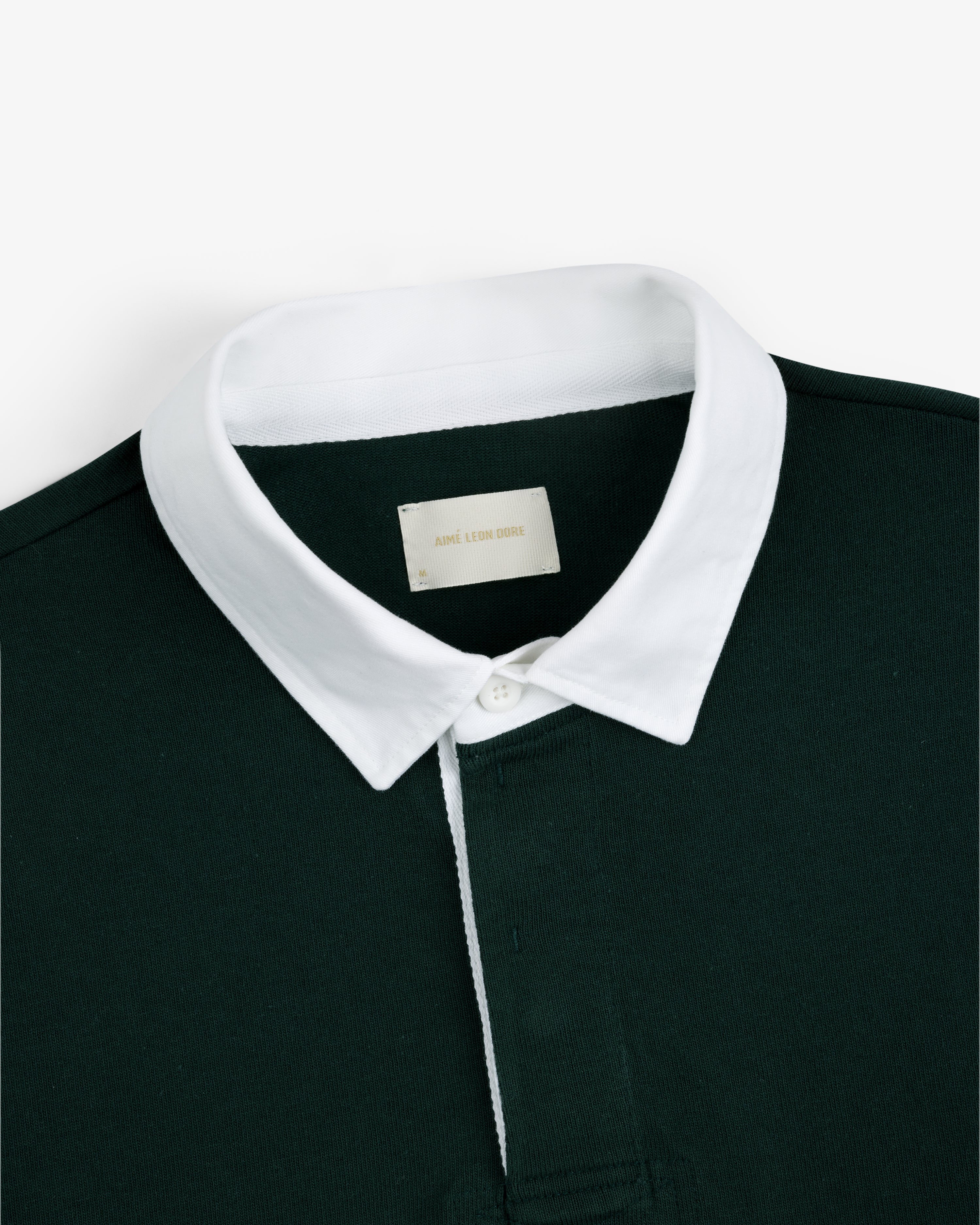 Script Paneled Rugby in dark green with a white collar and visible neckline label, shown on a plain background.