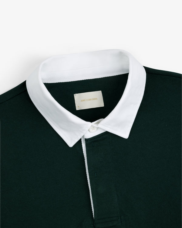 Script Paneled Rugby in dark green with a white collar and visible neckline label, shown on a plain background.